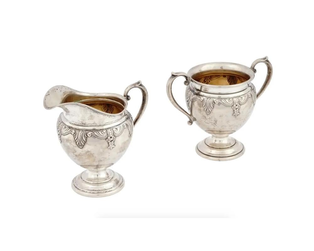 An antique American Wallace sterling silver footed sugar bowl and creamer, each featuring a Stradivari pattern with relief body decorations. Marked with the manufacturer and silver proof marks and numbered to the base. Circa the early 20th century.