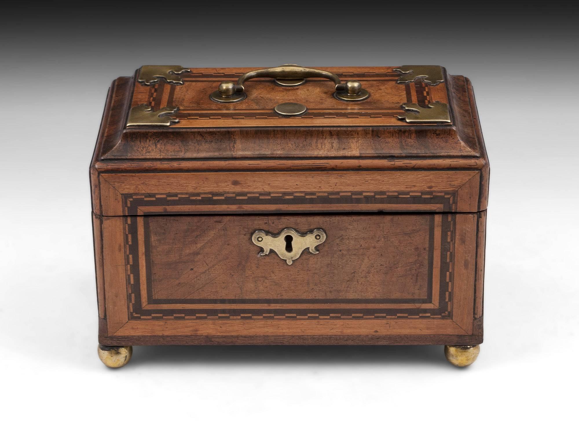 Antique tea caddy with brass handle, decorative edges, escutcheon and ball feet. 

Each side has a panel design with checkered borders. The interior has three compartments with traces of a decorative red finish. 

This tea caddy comes with a