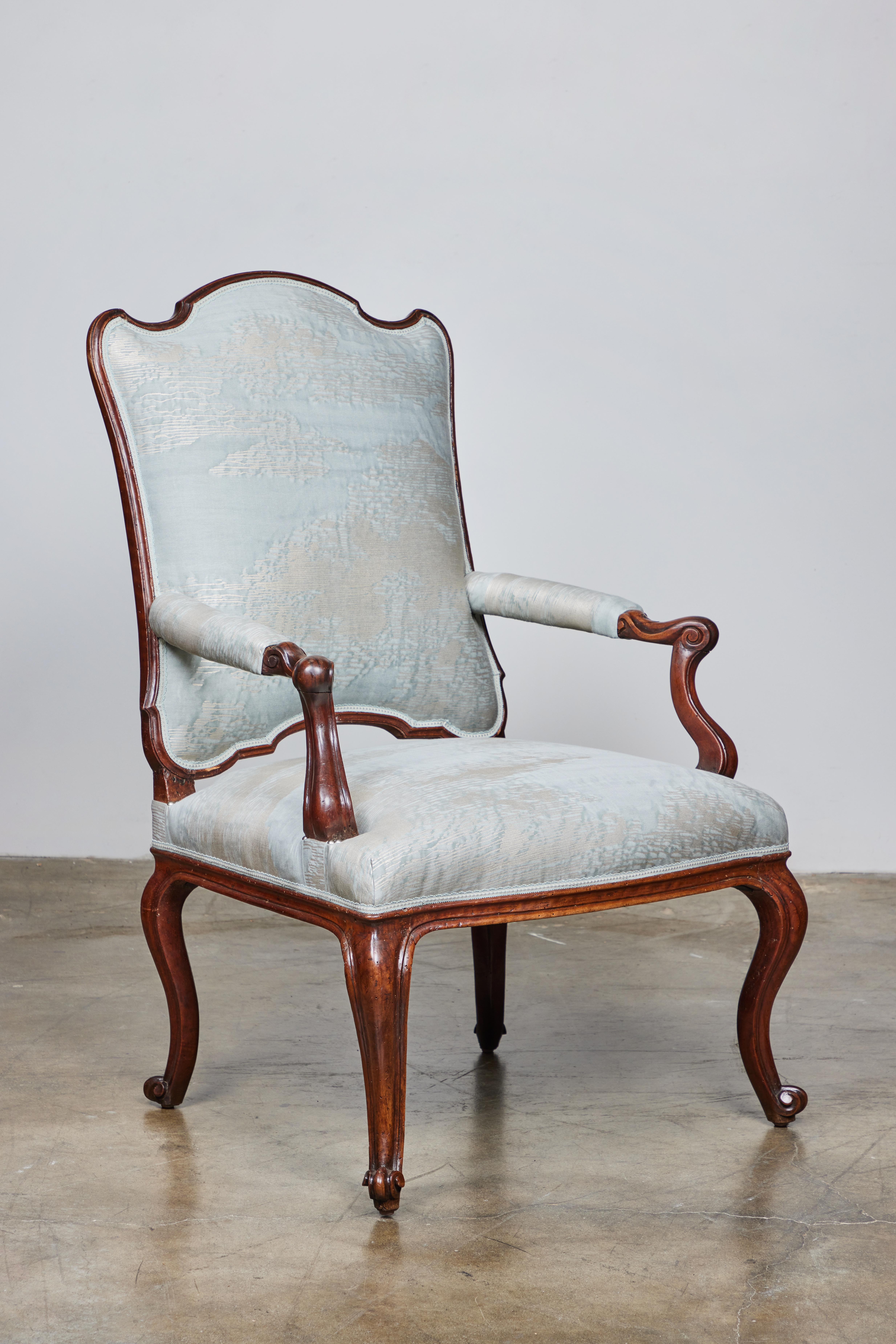 A beautifully carved walnut armchair newly upholstered in Fortuny fabric with trim and silver nail heads.
