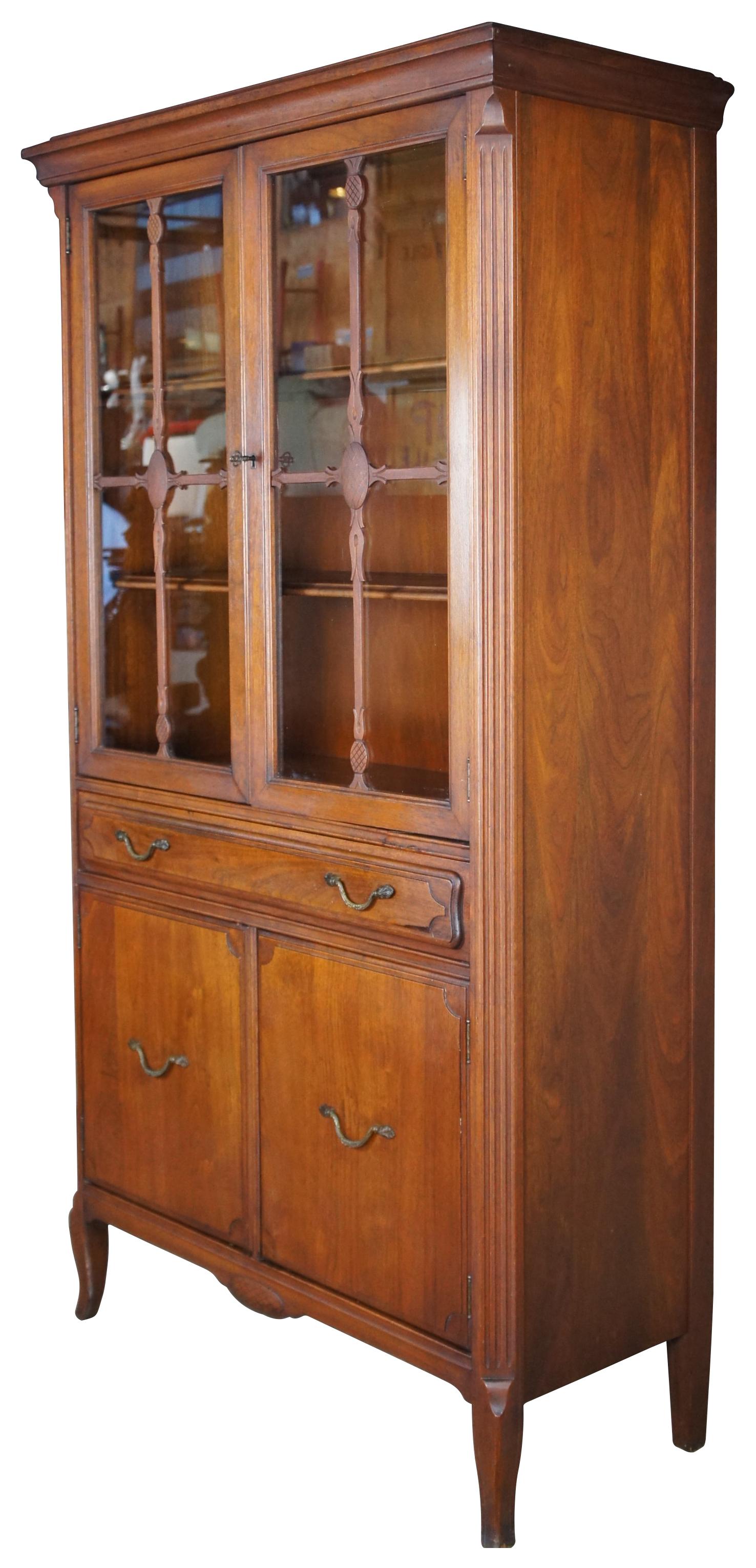 An Early 20th Century American display cabinet.  Made of walnut with rectangular form that features an upper cabinet with pineapple style lattice doors over one drawer and lower cabinet.  Includes Chamfered fluted stiles terminating into rams