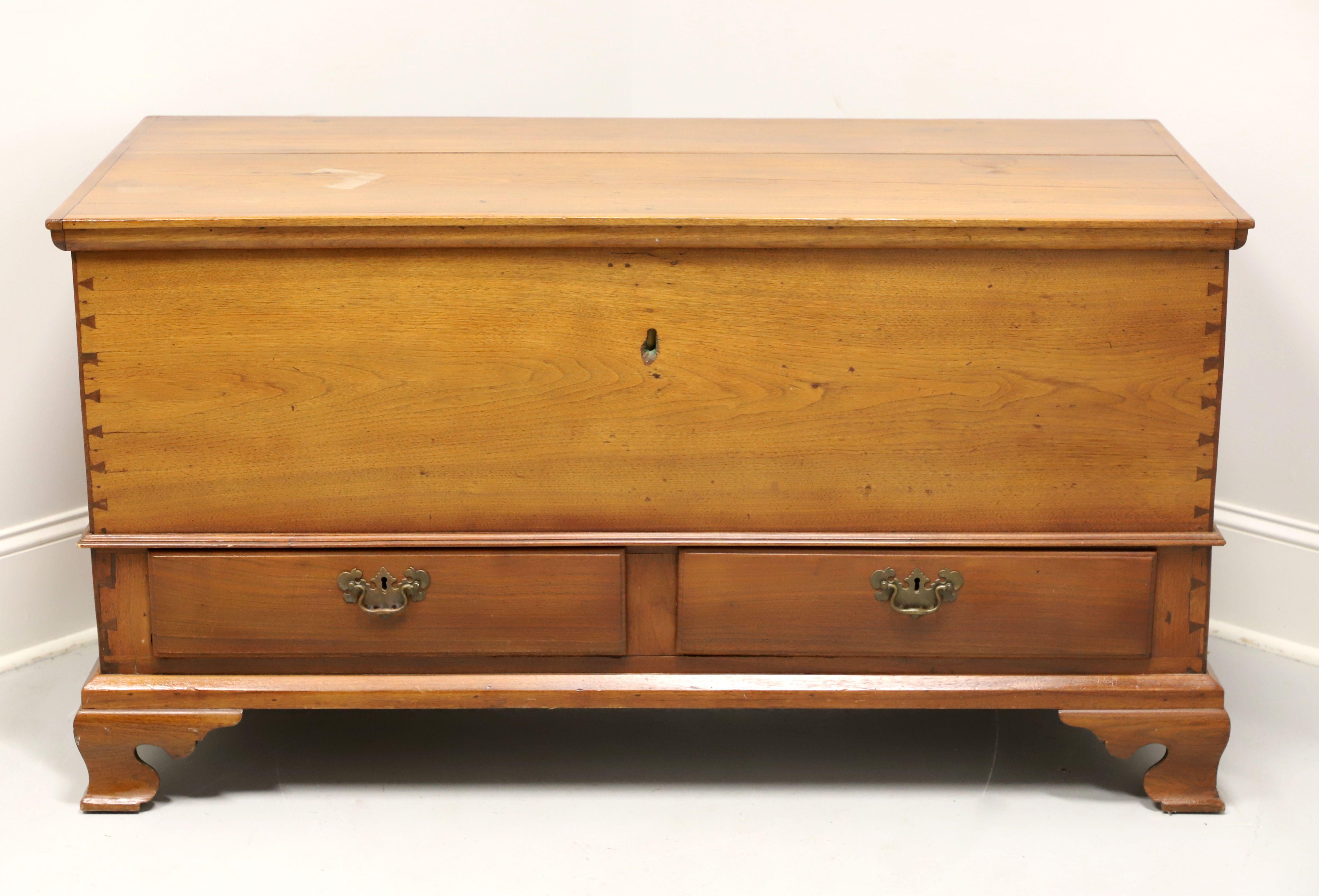 A large antique American Colonial style blanket chest, unbranded. Solid walnut with brass hardware, bevel edge to the lid top, hinge hardware holding the lid, decoratively exposed dovetail joints, lower drawer area, brass side handles, and ogee