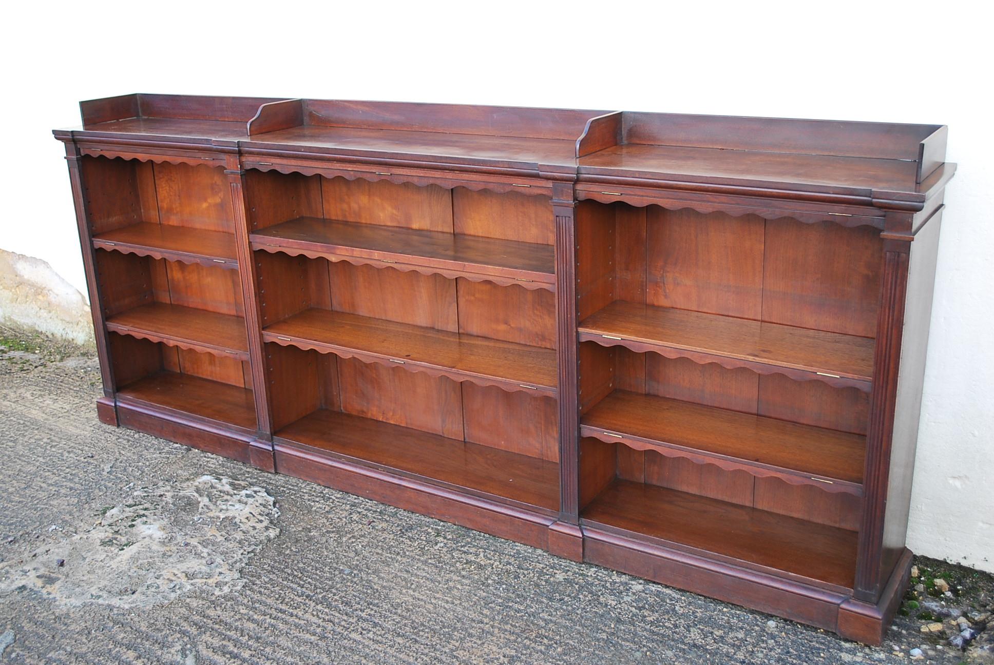 A good quality English breakfront open bookcase with adjustable shelves. Made in solid walnut with good color and patination. A rare example of its kind, with patented book dust covers that fold down rather than leather ones which deteriorate. An