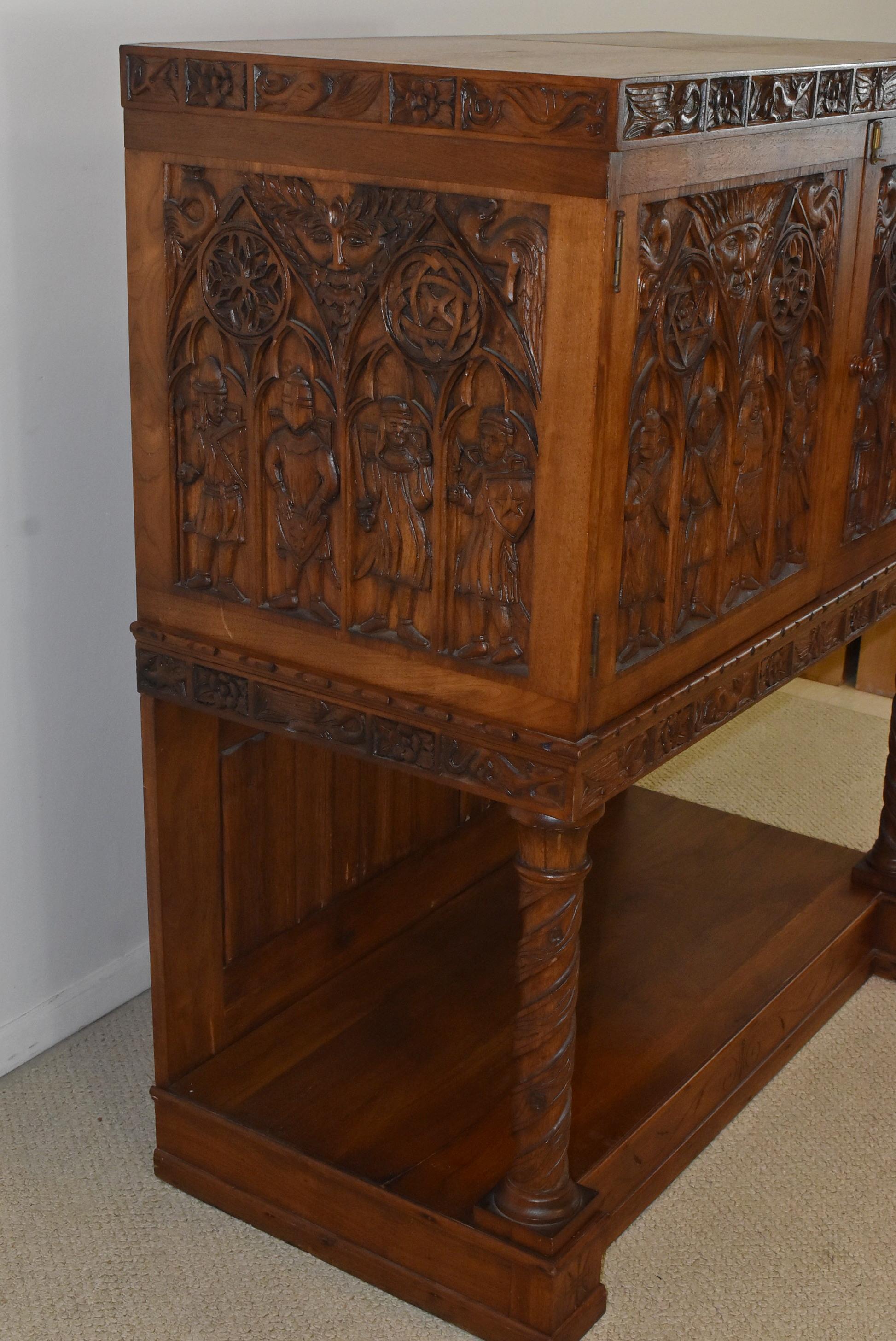 Antique carved walnut Gothic Revival liquor cabinet. Knights, birds, foxes and mythical faces depicted. Rope turned pillars with a bottom shelf. Draped carved back panels. Measure: 42