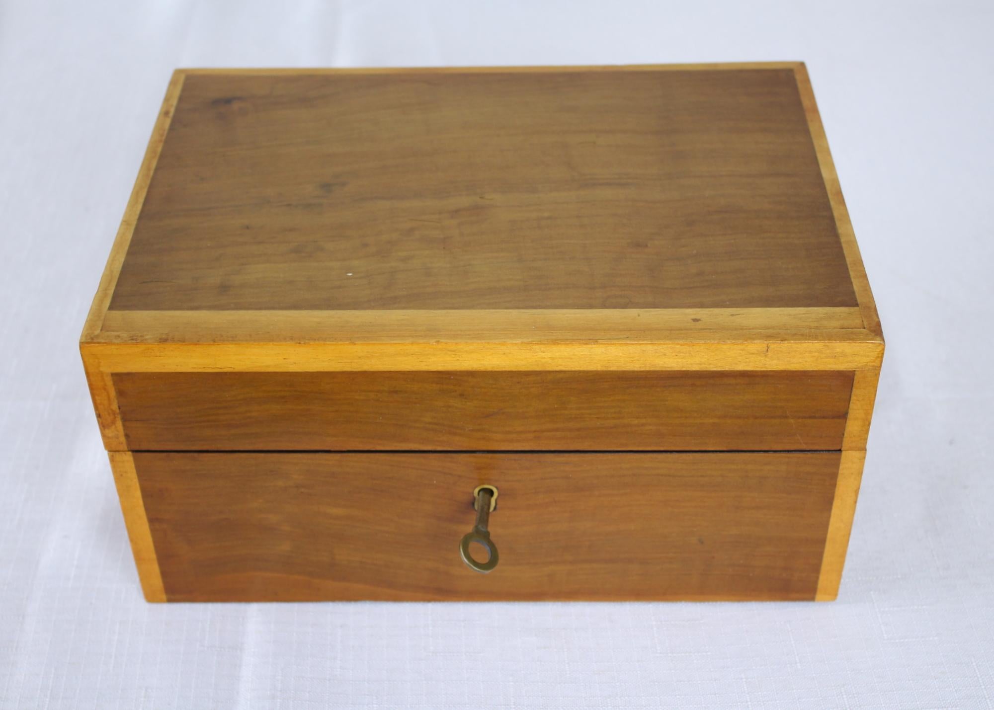 A lovely light colored walnut jewelry box with original working key. The satinwood crossbanding is in good condition and the interior of the box is clean with a green velvet bottom.