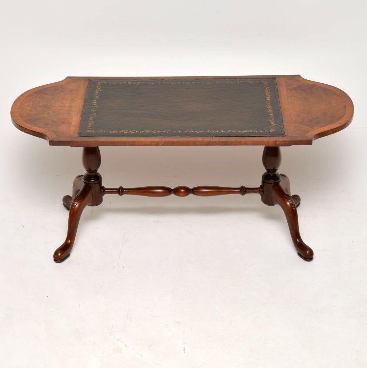 Antique walnut coffee table with a tooled leather in the middle and burr walnut panels inset in the shaped ends. It sits on twin pedestal legs, joined by a turned cross stretcher with two shaped legs carved on the knees with shell carvings. This