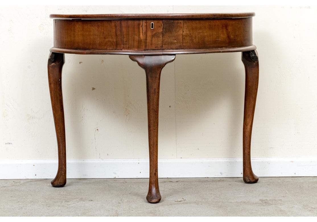 La table console démilune avec une large frise et un plateau élévateur avec un trou de serrure en laiton (sans la clé) ouvrant sur un espace de rangement. Il repose sur de hauts pieds incurvés, avec de larges genoux et des pieds à coussinets