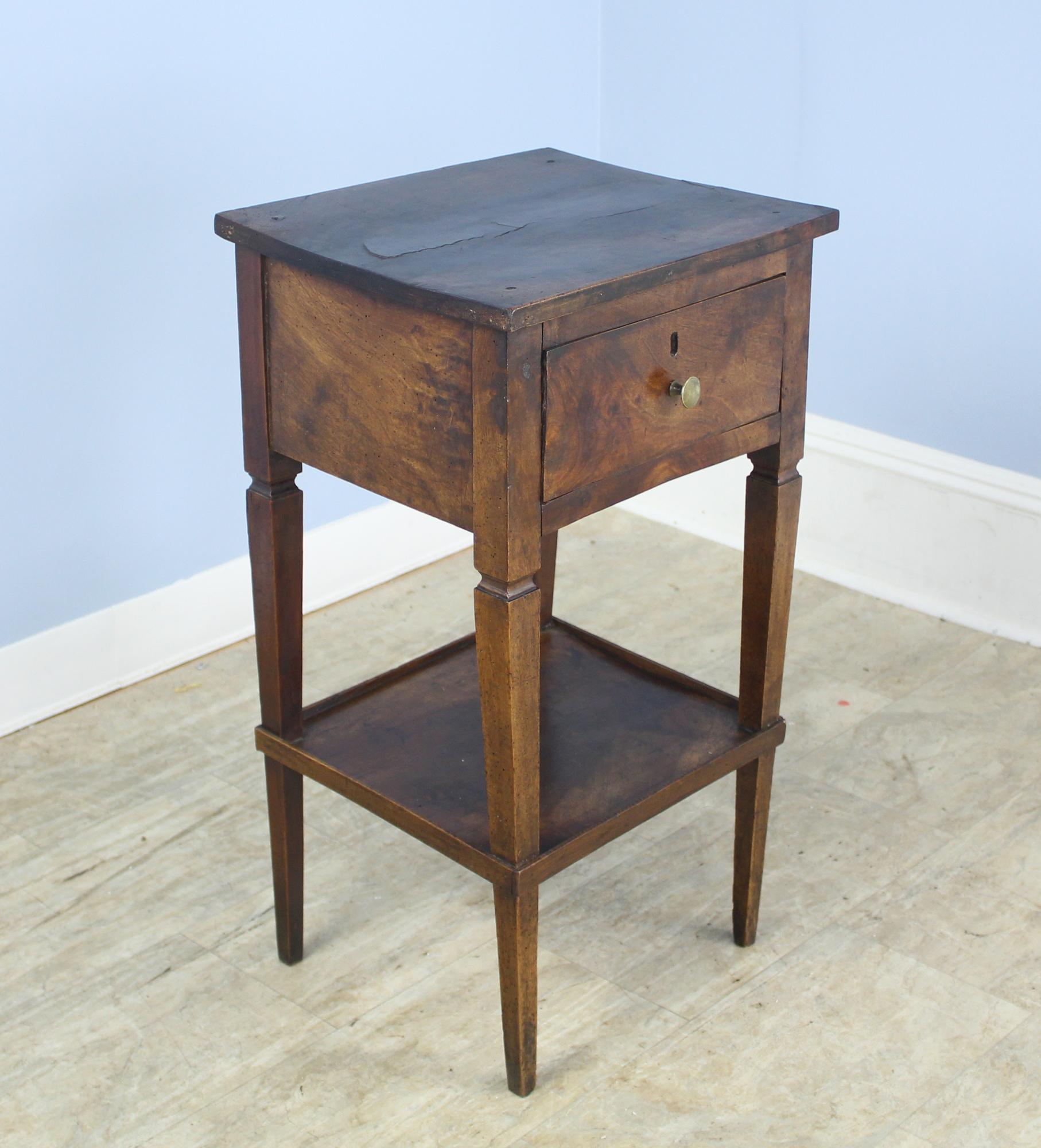 A lovely occasional table in dark patinated walnut. The top shelf is thick and has lovely walnut grain with a slight bow. The lower shelf adds a decorative element, and has little galleries to keep items from slipping off. Some distress and a