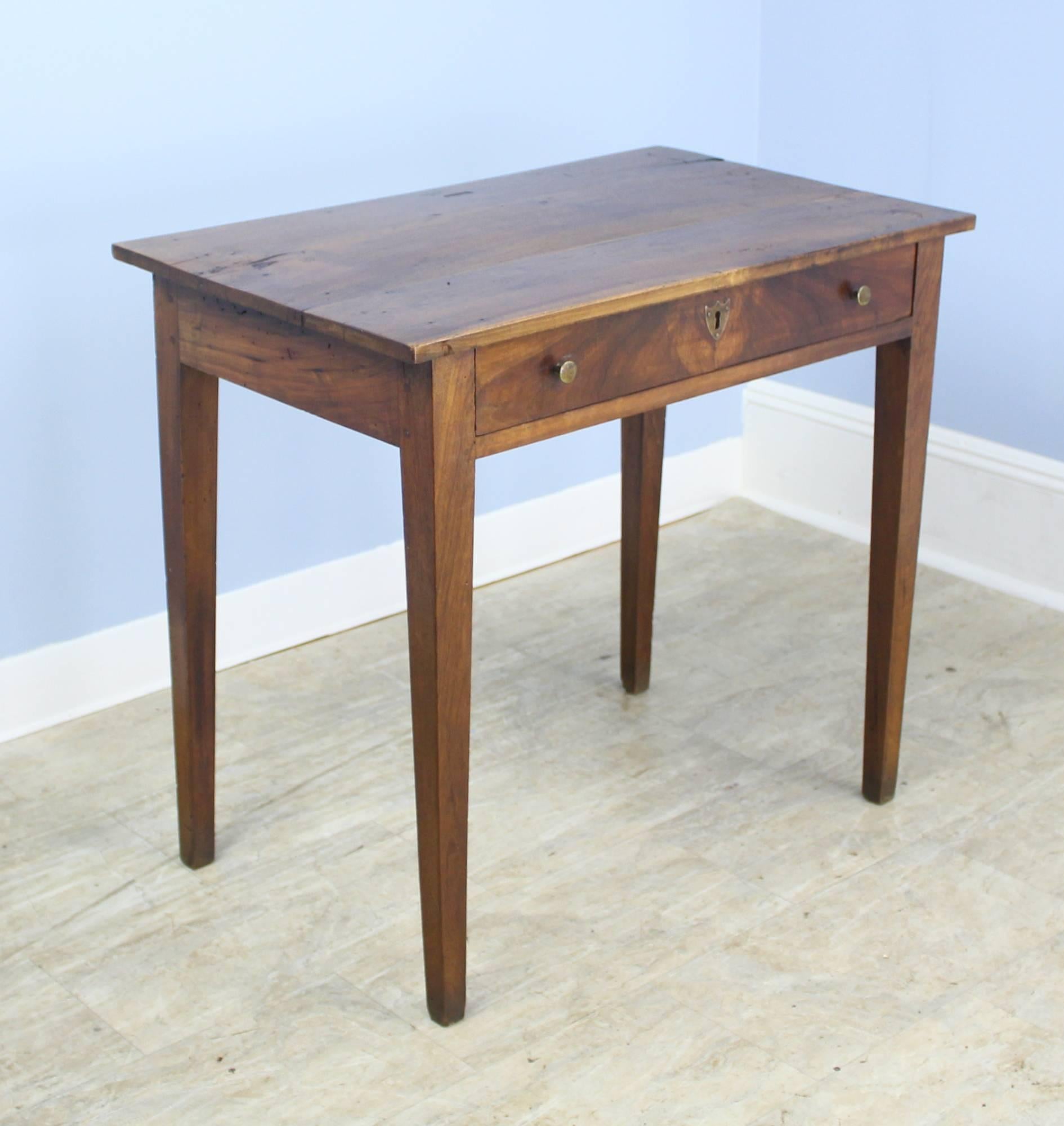 An elegant walnut side table with a beautifully grained top.  Single long drawer and long tapered legs. Beautiful patina and dramatic walnut grain. The large brass escutcheon on the drawer is eye-catching. A Classic!