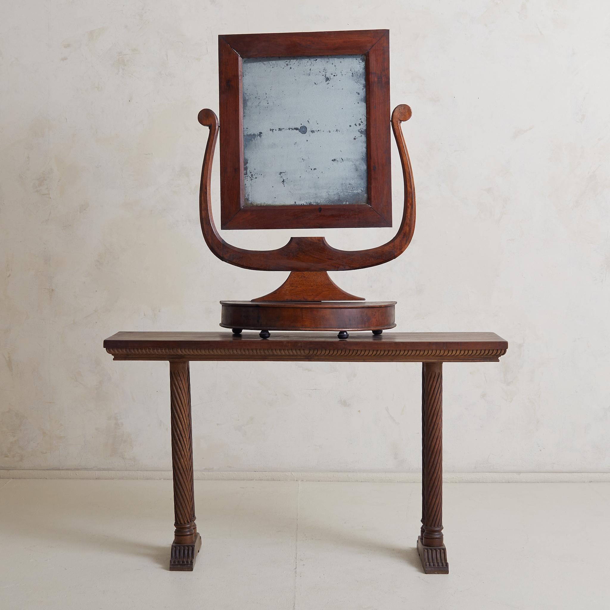 Un beau miroir de courtoisie ancien avec un cadre en noyer harpé et une base de piédestal démilunie. Le cadre supporte un miroir rectangulaire pivotant et repose sur quatre pieds en métal noir. Cette pièce présente une magnifique patine et une