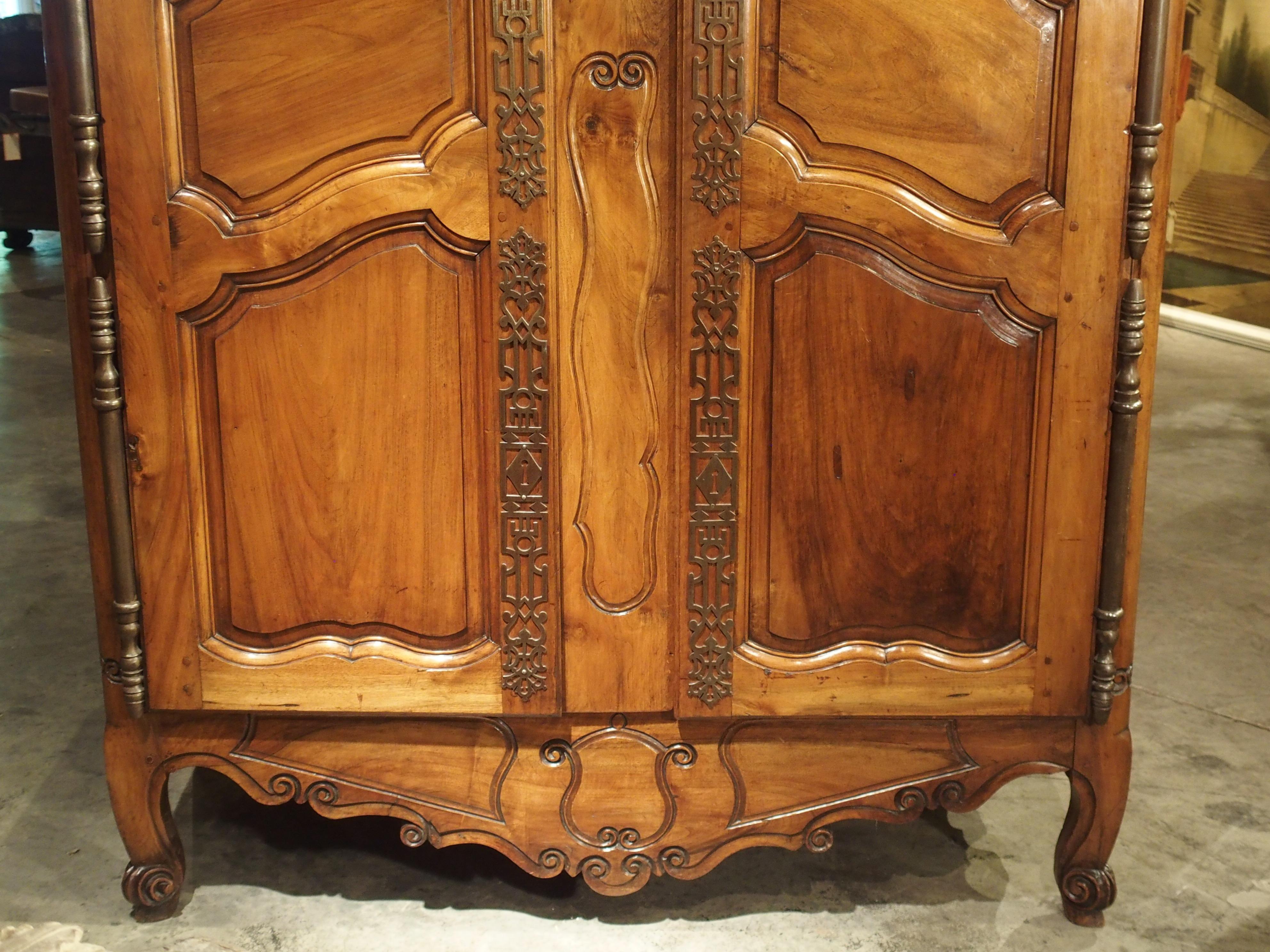 This elegant antique French armoire from Fourques, France is a masterpiece of balance in its design. It has very sparse yet deeply carved c-scroll motifs on all of the thick tri-partite walnut wood panels. This simplicity is balanced by ornate