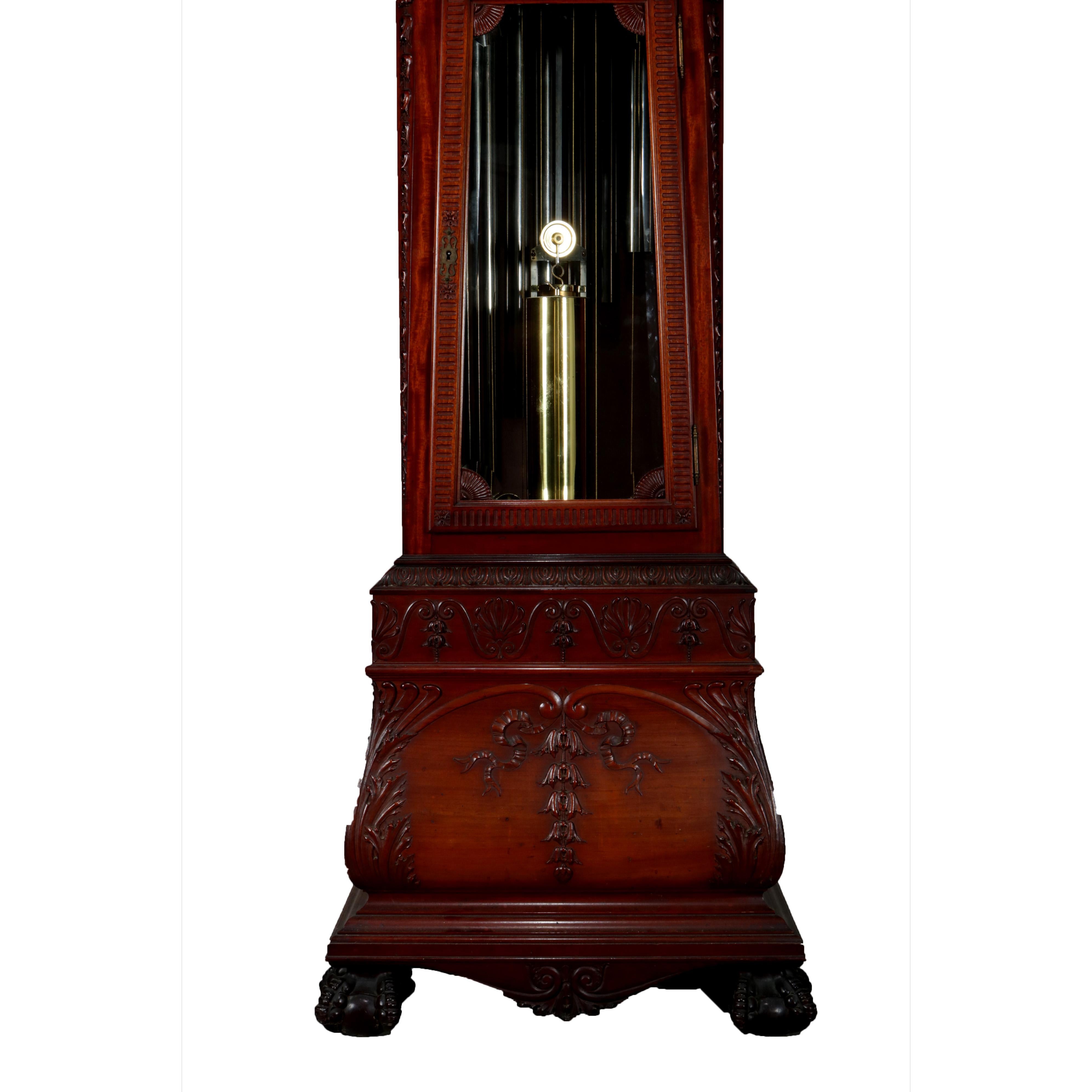 Antique tall case mahogany Walter Durfee grandfather clock features bonnet with broken arch pediment decorated having ribbon and inverted bellflowers with scrolled broken arch having rosettes and flanking central urn surmounting waist with flared