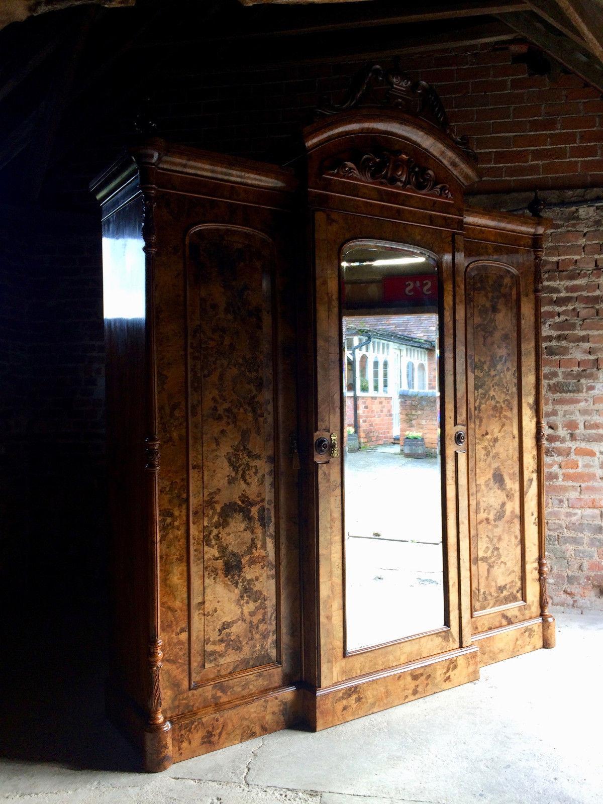 A mid-Victorian figured and painted walnut breakfront wardrobe carved urn and broken arch pediment, applied shallow arch panel with cartouche and leaf scrolls, over an arched and bevelled mirror door flanked by an arch panelled door to either side,