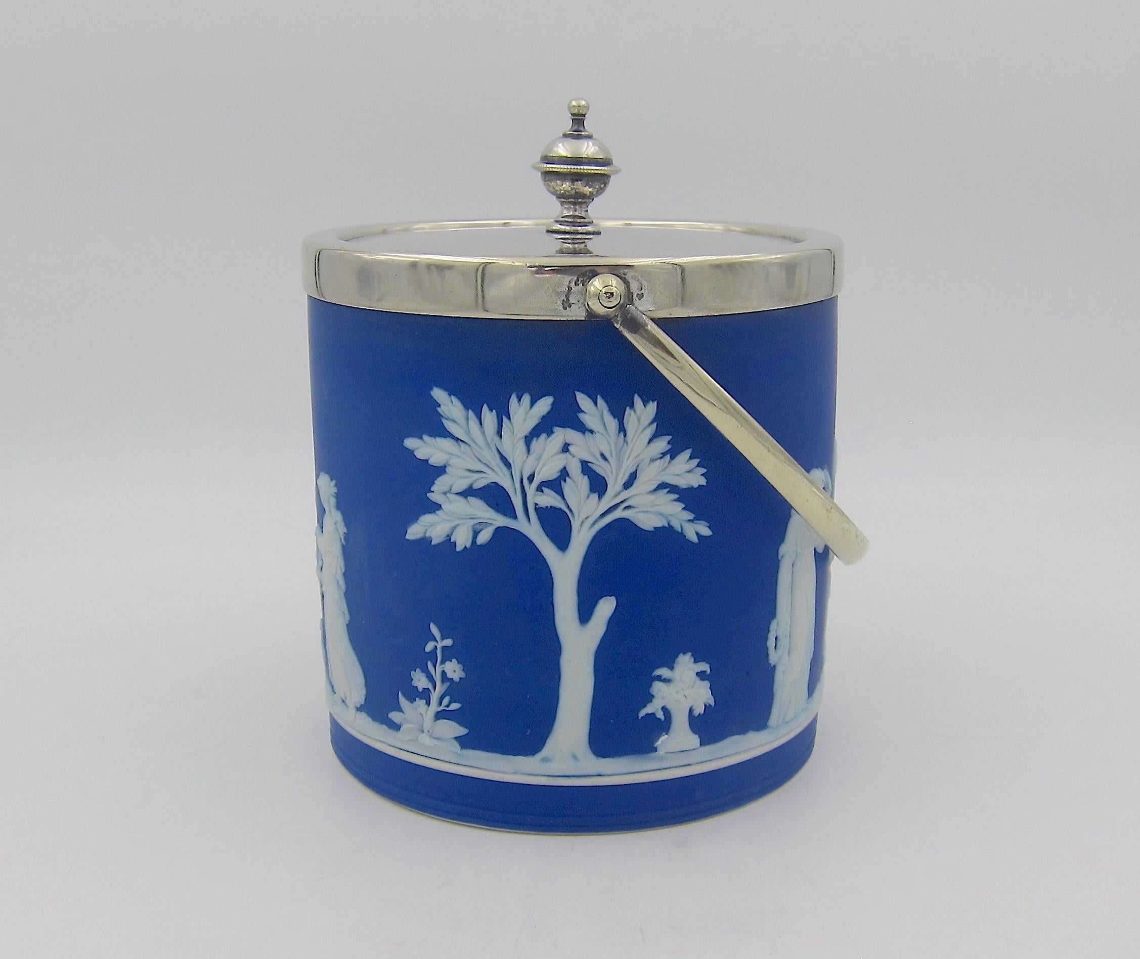 An antique Wedgwood biscuit barrel jar in deep blue jasper ware with white Neoclassical trees and sacrifice figures in relief. The cylindrical-shaped covered jar was made in England during the late Victorian era, circa 1880s to early 1890s. The