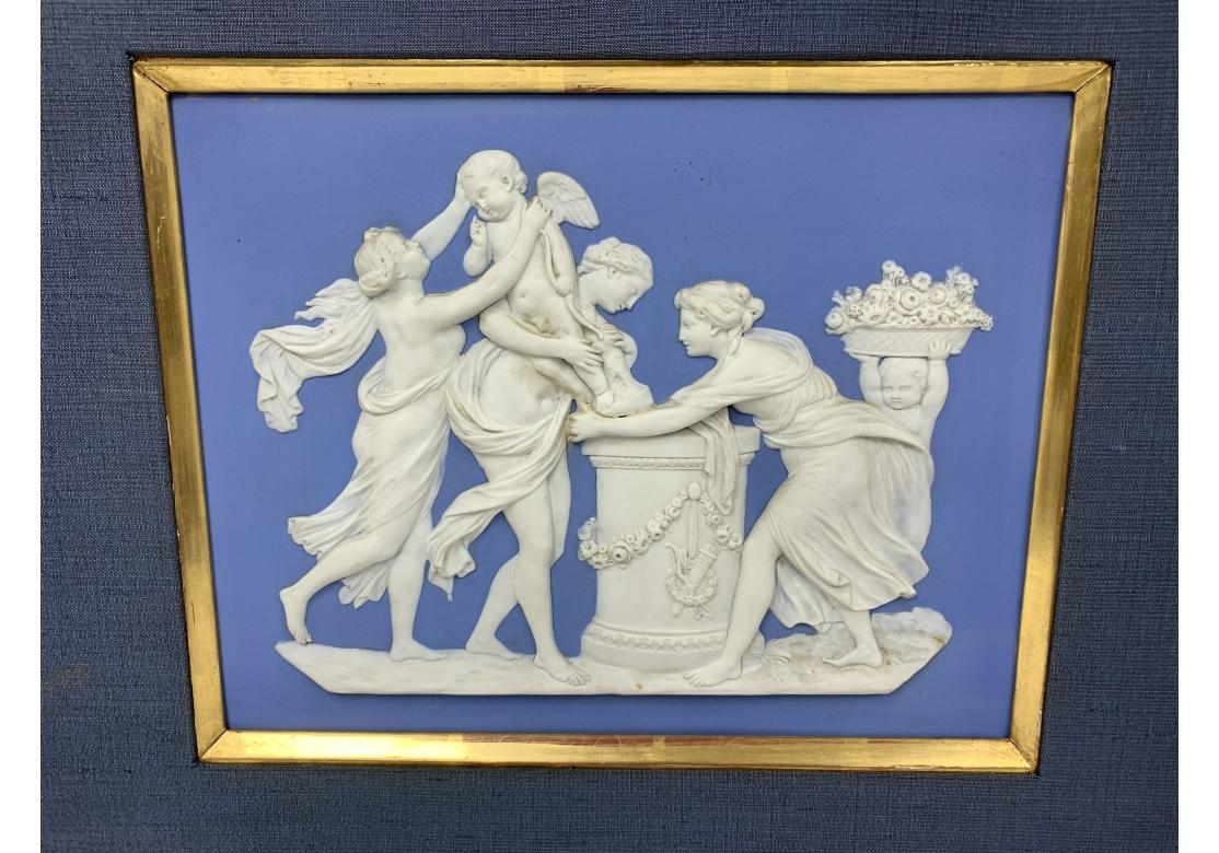 A fine Wedgwood blue jasperware plaque with a neoclassical figural composition. The Wedgwood impressed mark appears on verso. Female figures are honoring the devilish Eros who they are raising up to stand on a pedestal decorated with floral swags