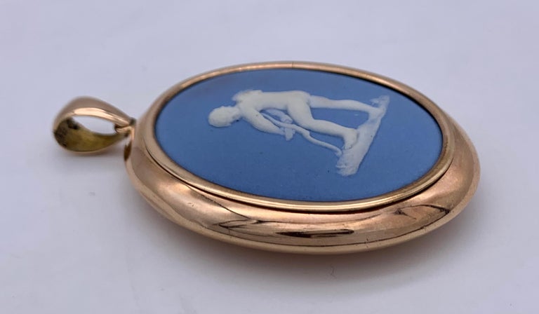 This Wedgwood cameo of amor carving his bow is set in a red gold oval closed pendant mount marked 9 karats. 