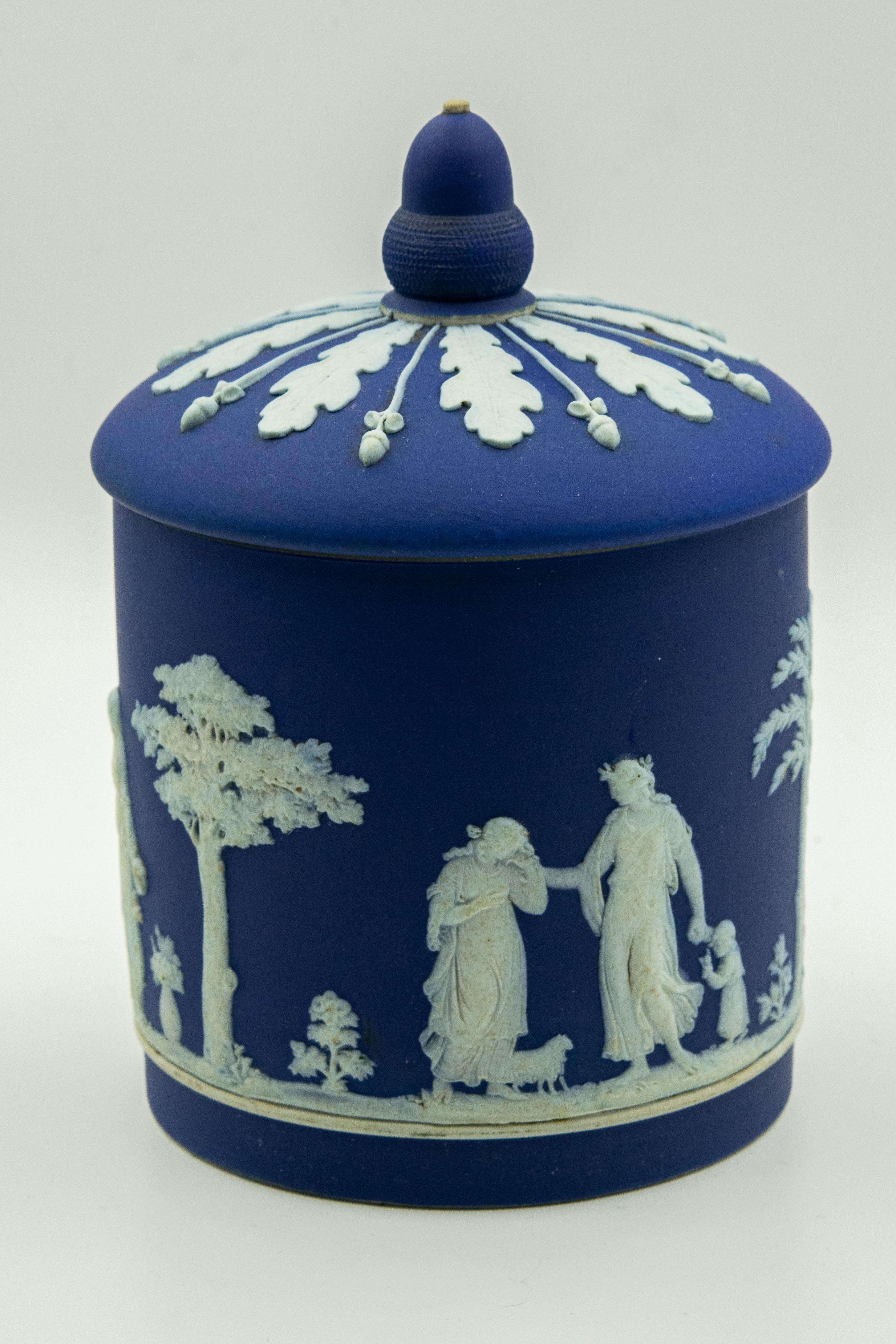 Antique dark cobalt blue dip Wedgwood jasper ware biscuit barrel featuring a sprig moulded decoration which shows neoclassical figures. The scene contains women, children and animals among trees and flowers. The lid is decorated with a wide band of
