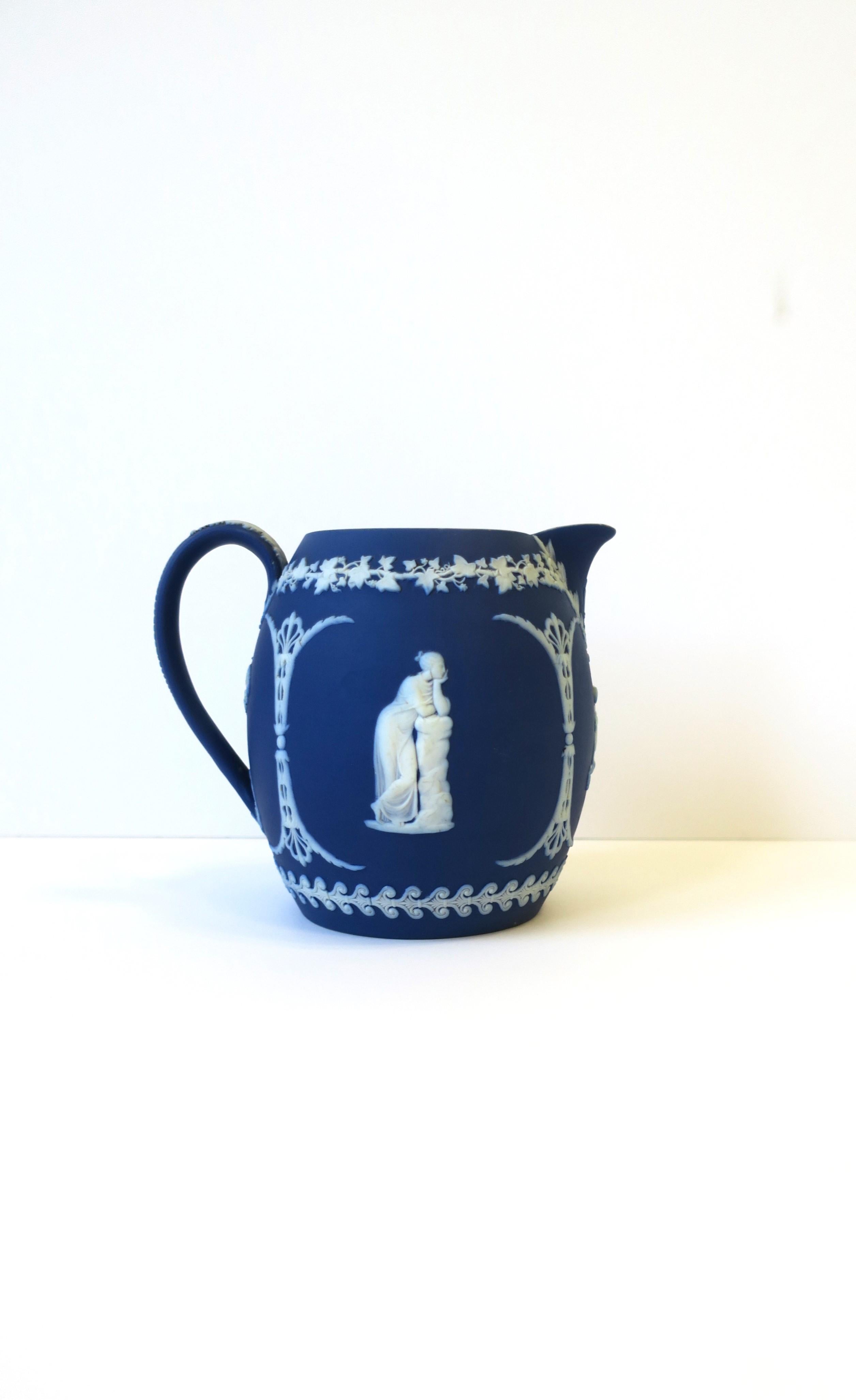 A beautiful antique English Wedgwood Jasperware blue and white pitcher, in the Neoclassical style, circa late 19th century, England. A beautiful matte unglazed stoneware pitcher or vase with a white raised relief; center area on two sides has