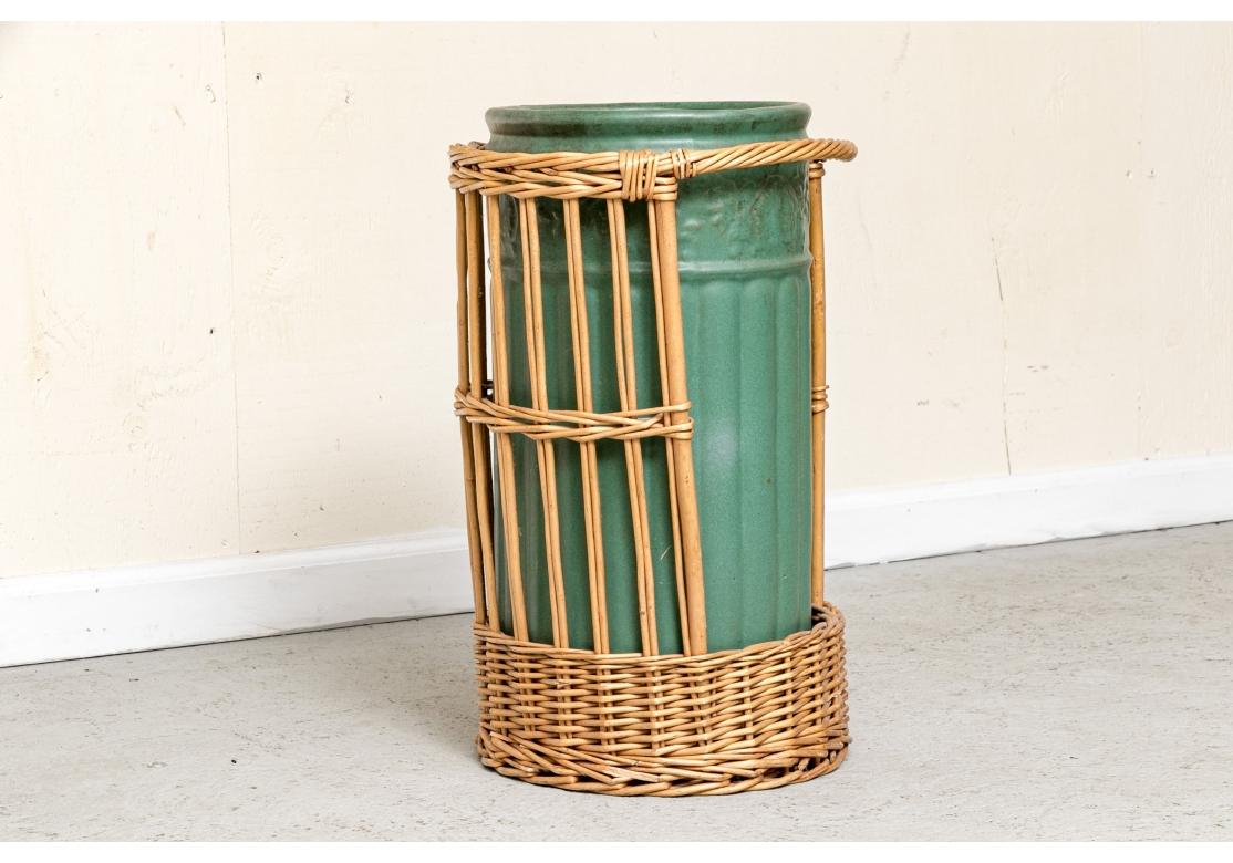 An antique umbrella/cane stand by Weller Pottery circa early 20th century. The pottery stand with relief floral and scroll border and reeded body. The stand is unmarked. Comes with a conforming wicker caddy with front opening exposing the stand to