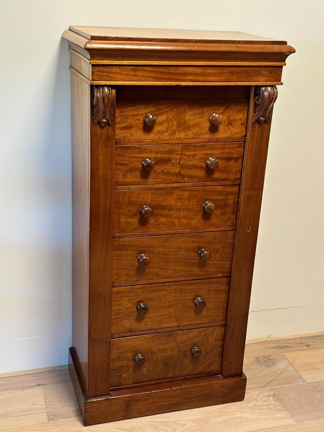 Here we have an antique English mahogany Wellington chest of drawers. In a beautiful original condition with a warm color. With its graceful design, rich mahogany wood and characteristic shape, this chest of drawers is not only a practical storage