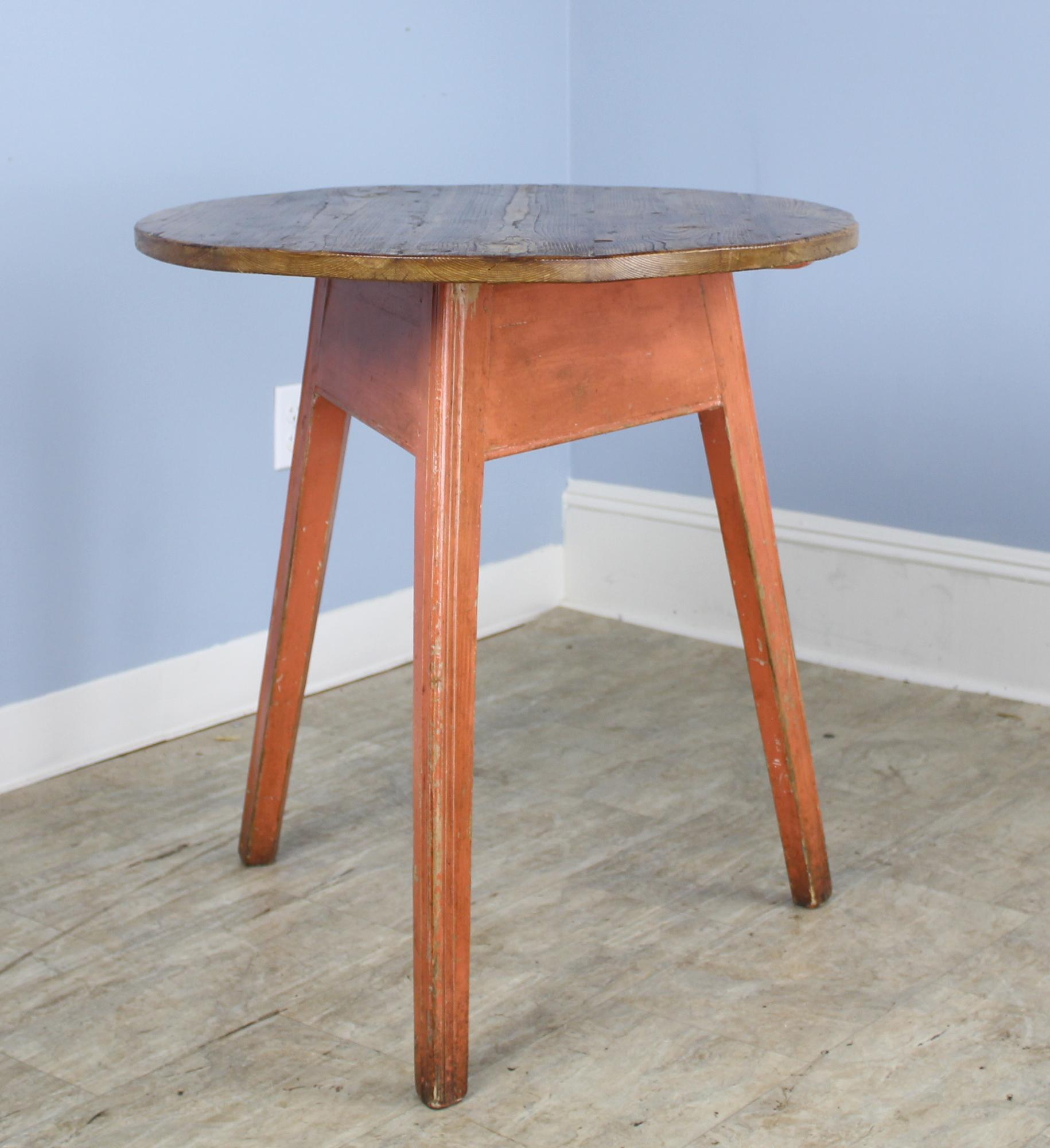 An antique Welsh cricket table. The base has the old light red paint, and the top is a honey pine, both rich in wear and patina. Makes a terrific lamp table. Note that the top is not a perfect circle.