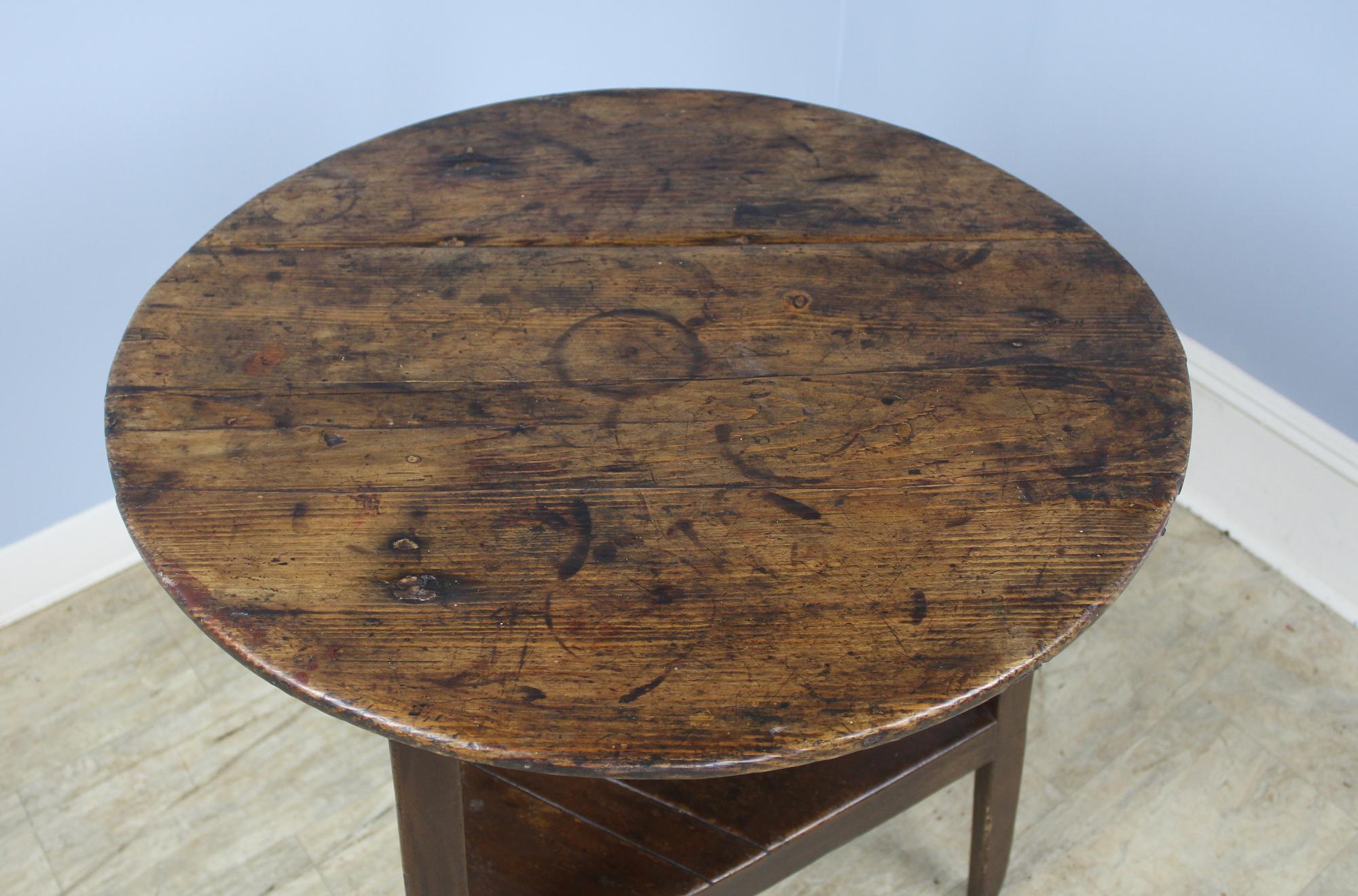A Welsh oak and pine cricket table with an extravagantly distressed and grained top for a dramatic country look. Typical three-legged table, with each leg having just three sides, and a shelf below. Excellent height for a lamp table, end table or