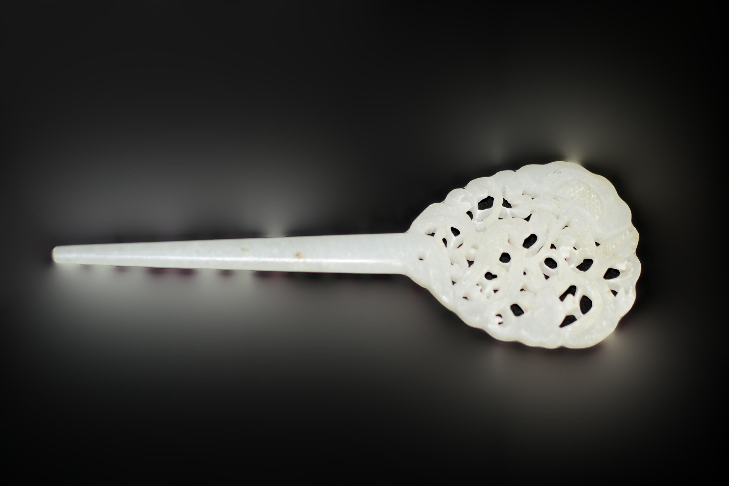 This beautiful white jade hair pin is a work of art. An oval head with scalloped edges is fully carved in three dimensions, showcasing an elegant peasant perched among the branches of a blooming prunus tree. The peasant, a symbol of a lady's regal