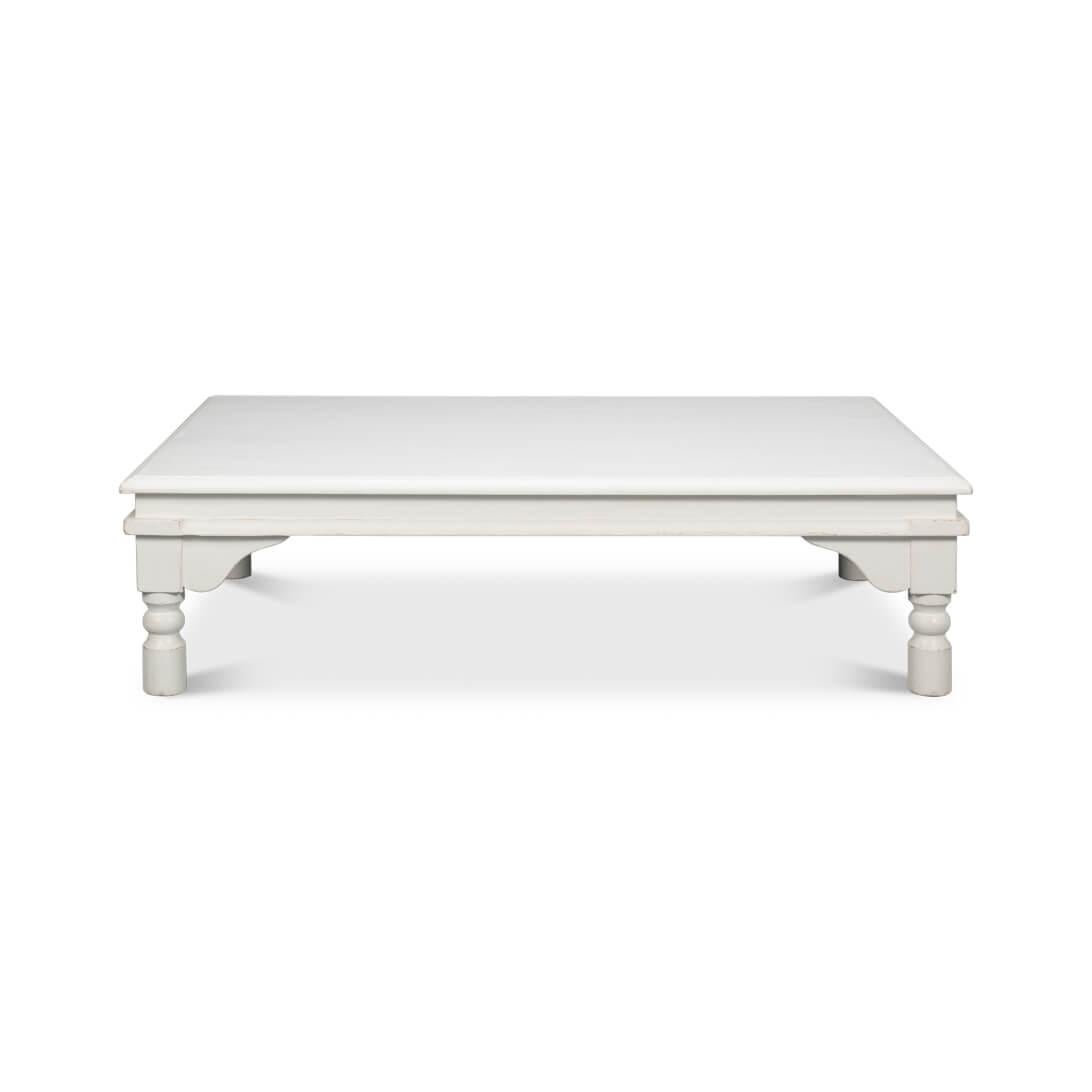Bathed in a soft, matte antique white finish, this table exudes a serene, welcoming vibe. Its substantial, low-rise design makes it a perfect anchor for your seating area, inviting leisurely conversations and cozy gatherings. 

The turned legs add a