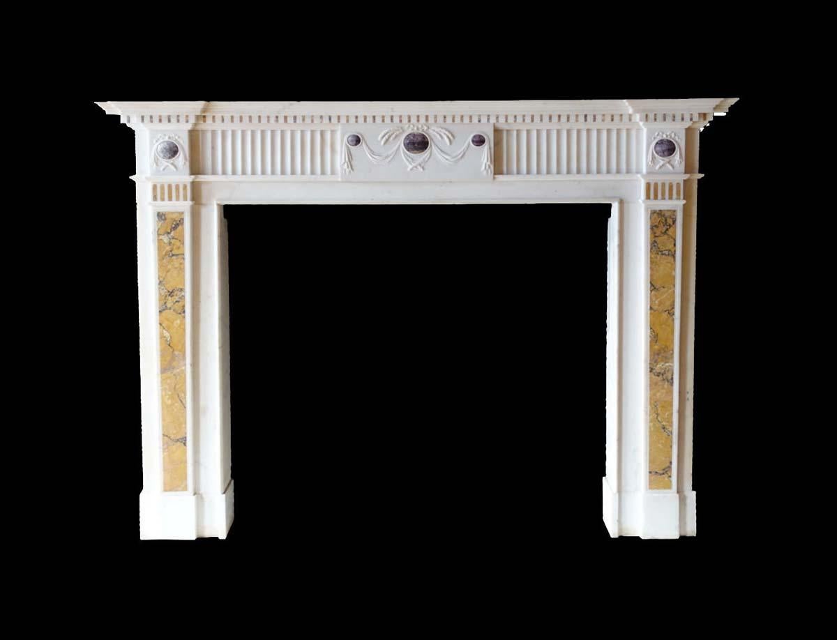 Cette cheminée en marbre de style Feder est magnifiquement sculptée dans un marbre blanc très légèrement veiné de gris. La cheminée est rehaussée d'une incrustation de marbre terre de sienne insérée de façon complexe entre les moulures dentaires