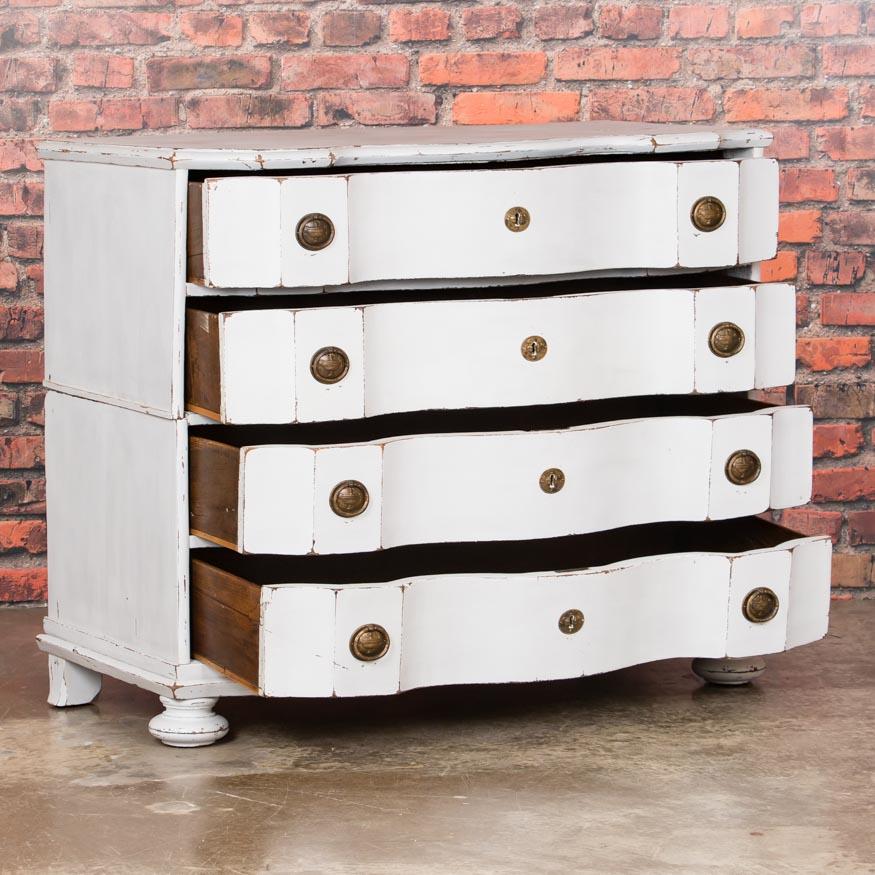 The strong visual appeal of this handsome Danish chest of drawers is due to the lightly worn white paint and the clean, curved lines. Where the paint has been gently scraped, the rich antique oak is revealed adding to the aged character and