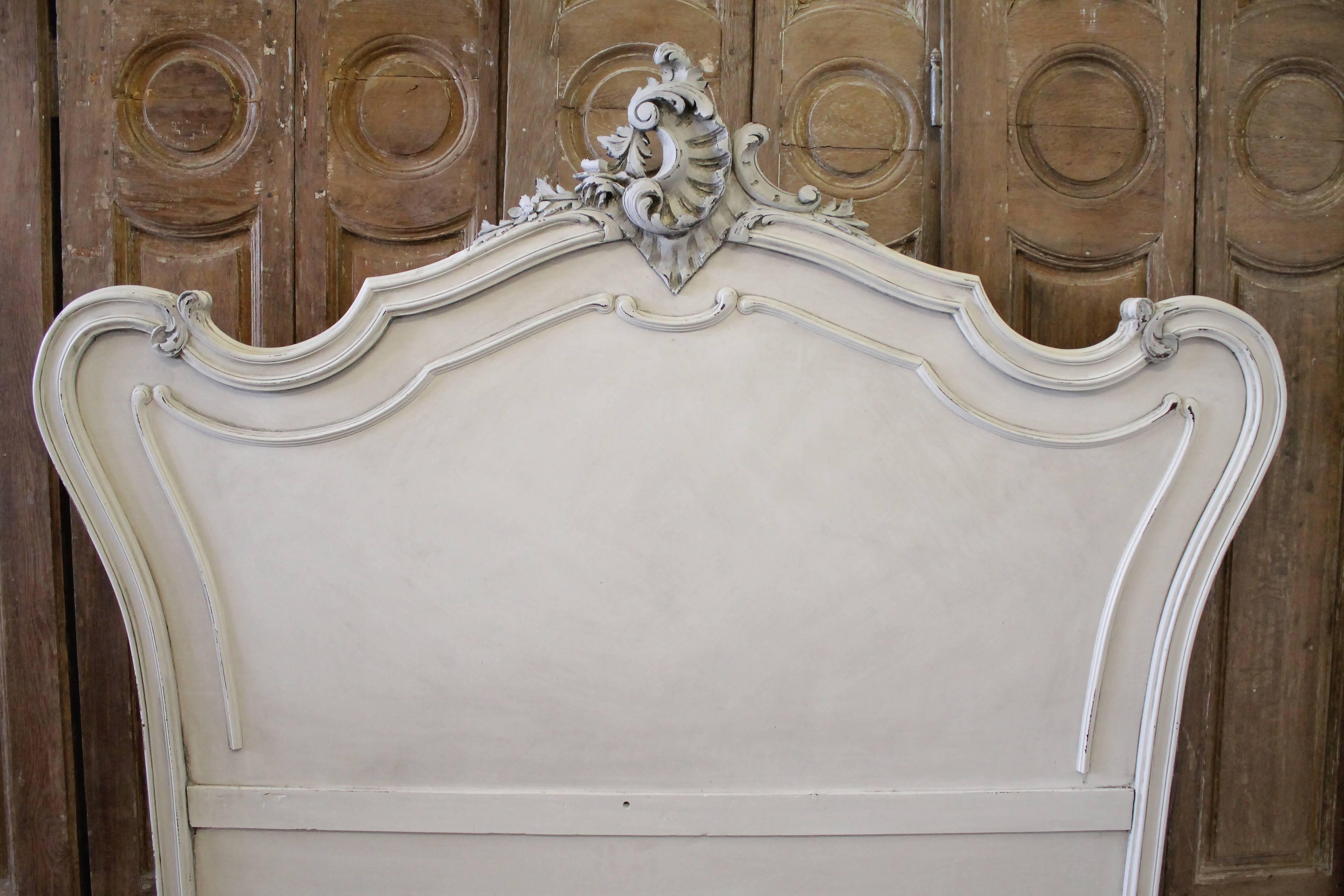 Antique white painted French Louis XV style walnut carved queen French bed
This bed was painted in an antique oyster white color with accents of French grey, slightly distressed patina, and finished with an antique glaze.
A large carved cartouche