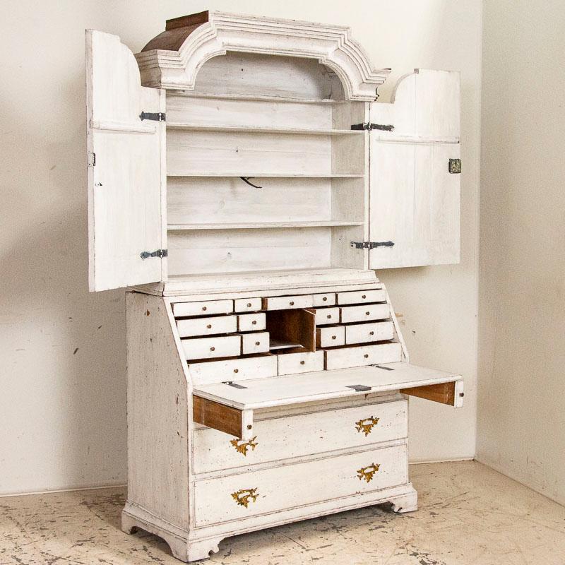 Stately and elegant, this tall white Gustavian pine secretary shows off with the distinctive shape of the top bonnet or crown. Also known as a bureau, this secretary would have been a 