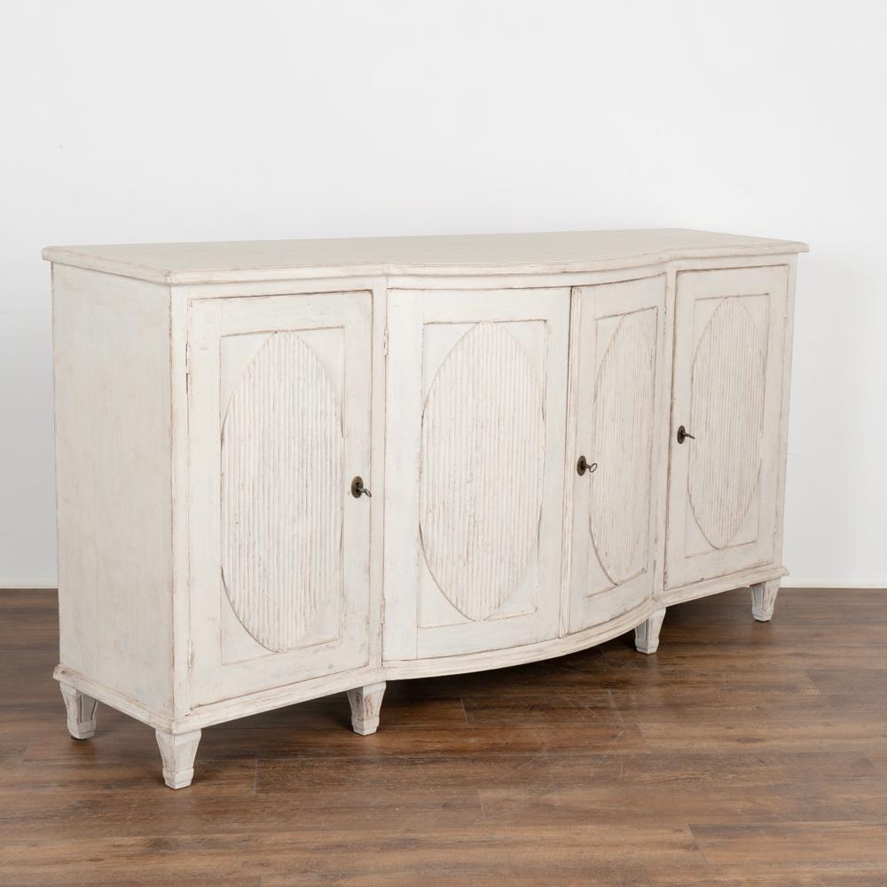 Swedish 6' long gustavian sideboard buffet server with four cabinet doors.
Fluted large oval panel detail on each of the four doors, center two bow outward.
Tapered fluted feet. Three functioning keys included.
Later professionlly applied white