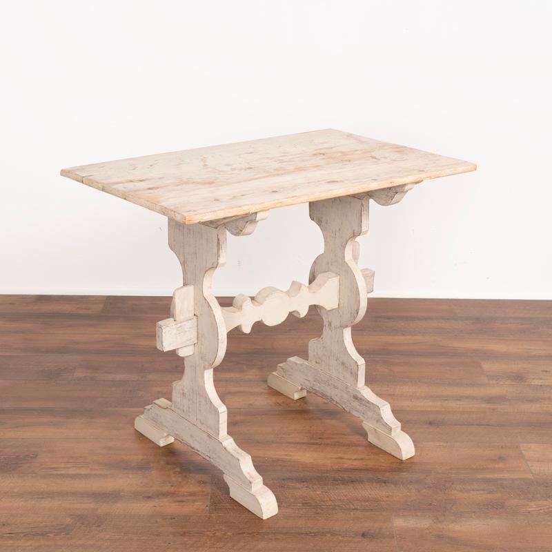 This small side table is both unique and charming, thanks to the gently distressed white painted finish and the decoratively carved trestle style base. This table has been restored, so it is strong, stable and ready for use. Any nicks, scratches,