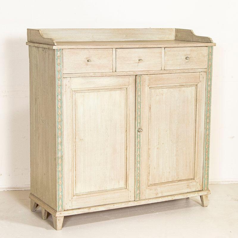The delight one finds in this sideboard is due to the soft painted finish. Newer professionally painted with a mix of whites accented by aqua blue trim along delicate carving create a cheerful feel to this pine sideboard. Look closely at the photos