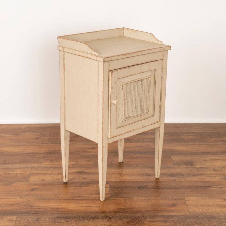 This petite white painted side table has the simple yet elegant lines that reveal its Swedish country style. The gentle tapered legs and vertical carving along the panel door were a traditional style motif reflecting the craftsmanship of the era.