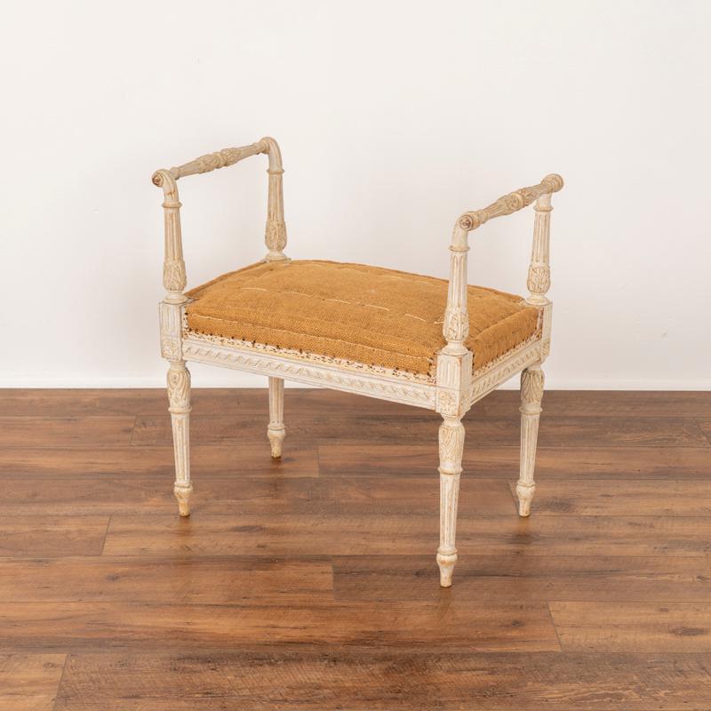 Swedish tabouret from the late 1800's. This enchanting stool is made with turned armrests or handles on each side as well as turned legs all accented with lovey carved details. The soft white paint has been lightly distressed adding an aged grace to