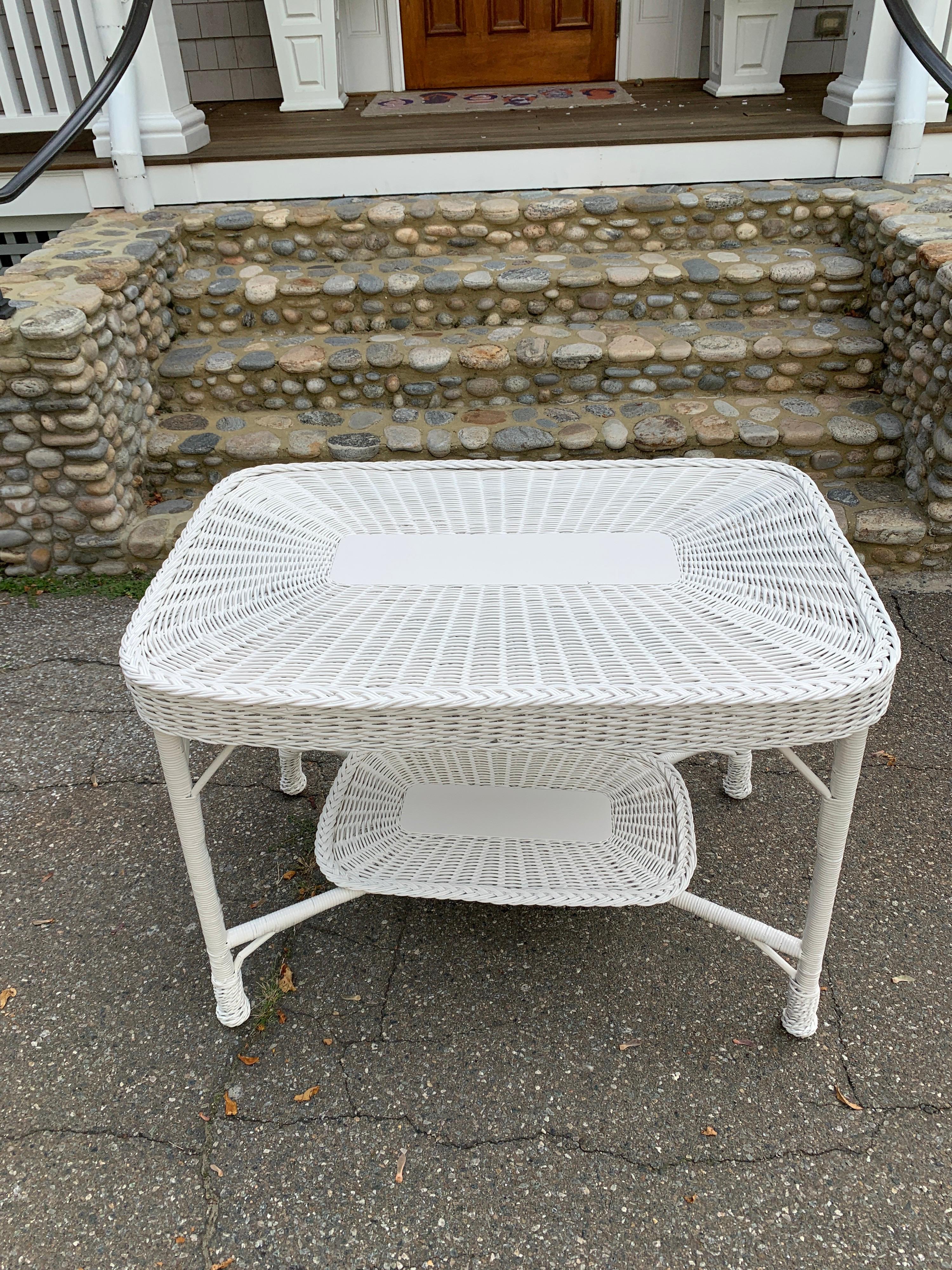 An antique white wicker table woven of reed with full woven apron and lower shelf. This is a substantial and sturdy piece. This piece measures 41