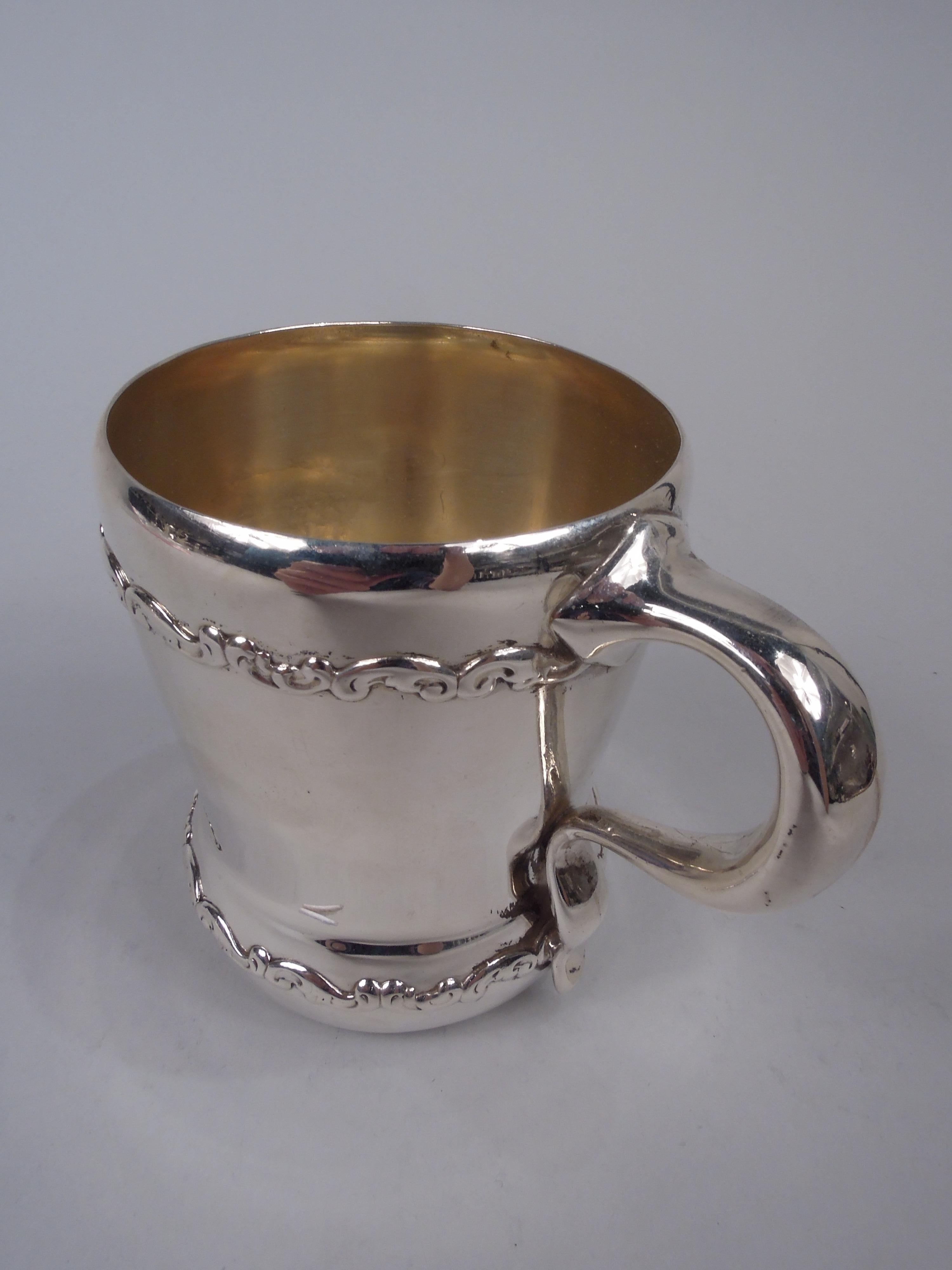 Edwardian Classical sterling silver baby cup. Made by Whiting in New York, ca 1910. Tapering sides, curved rim, and bellied bowl; c-scroll handle with scrolled tail. Two scrolled bands applied to top and bottom. Gilt-washed interior. Plenty of room