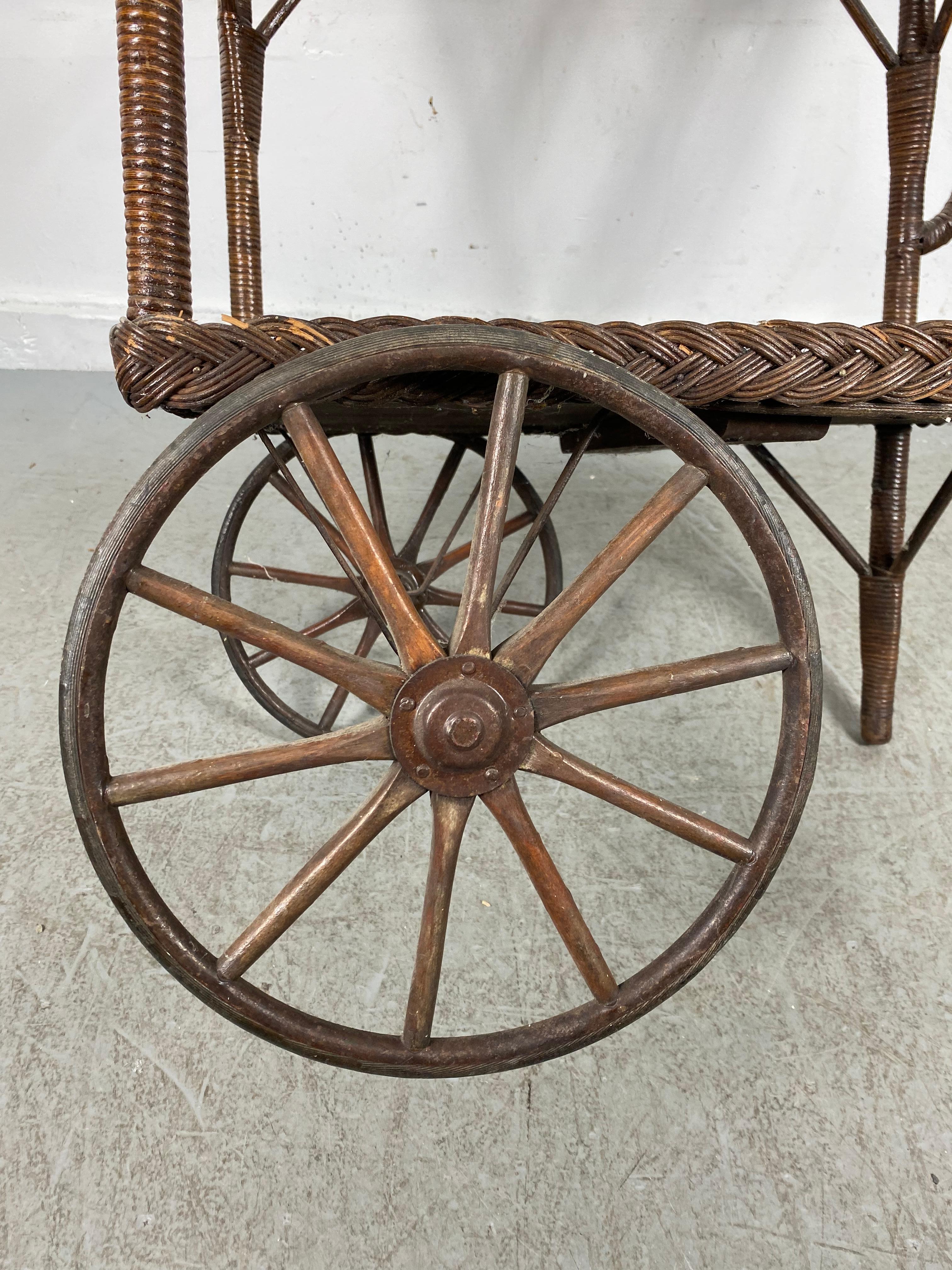 Nice early. Quite charming 2 tier bar or tea cart. Turn of the century, Great patina! Just the perfect amount of wear. Features two large iron spoke wheels, wood shelves, some wicker rap missing from right side of handle, Hand delivery avail to New