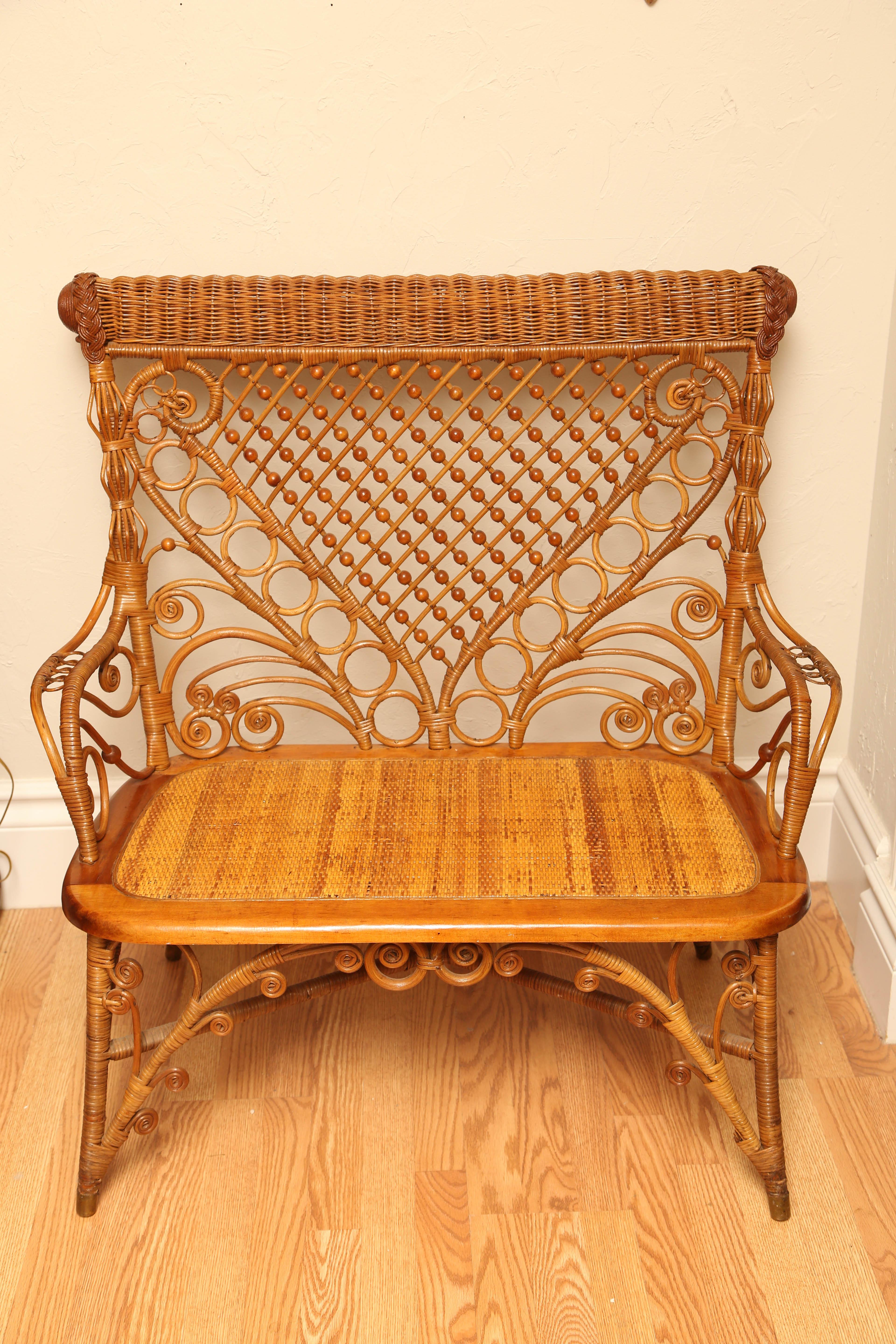 Charming antique wicker settee with a set in cane seat and ornate back and arms.