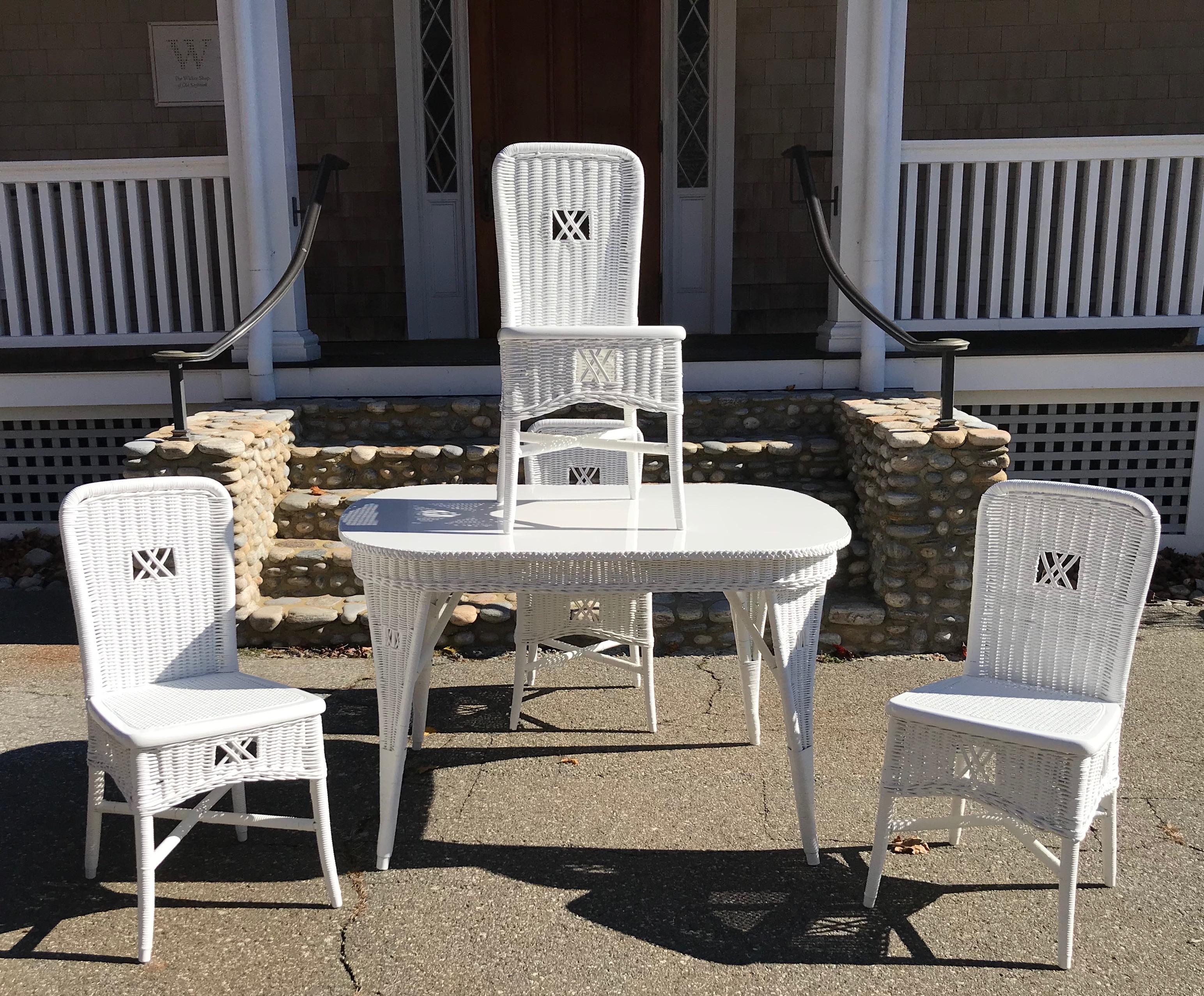 Antique wicker dining table and four chairs in fresh white paint. Solid wood top with woven reed skirt and woven legs on the table. Four matching woven reed chairs.