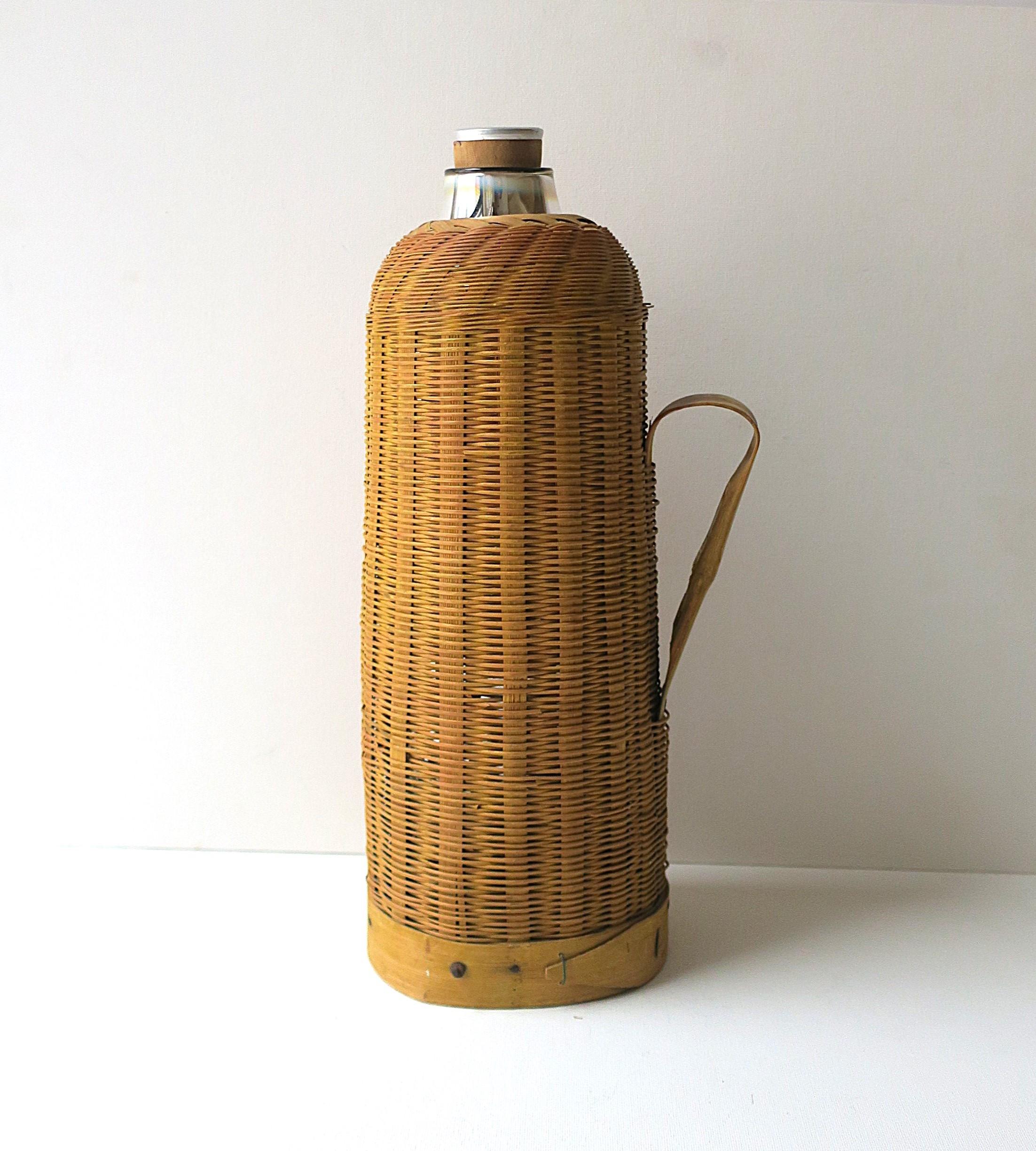 An antique wicker and mercury glass thermos pitcher, circa early-20th century, China. Beautiful wicker casing around a silver mercury glass thermos with silk, cork and aluminum stopper. Use as it was intended for, or as a decorative object. Very