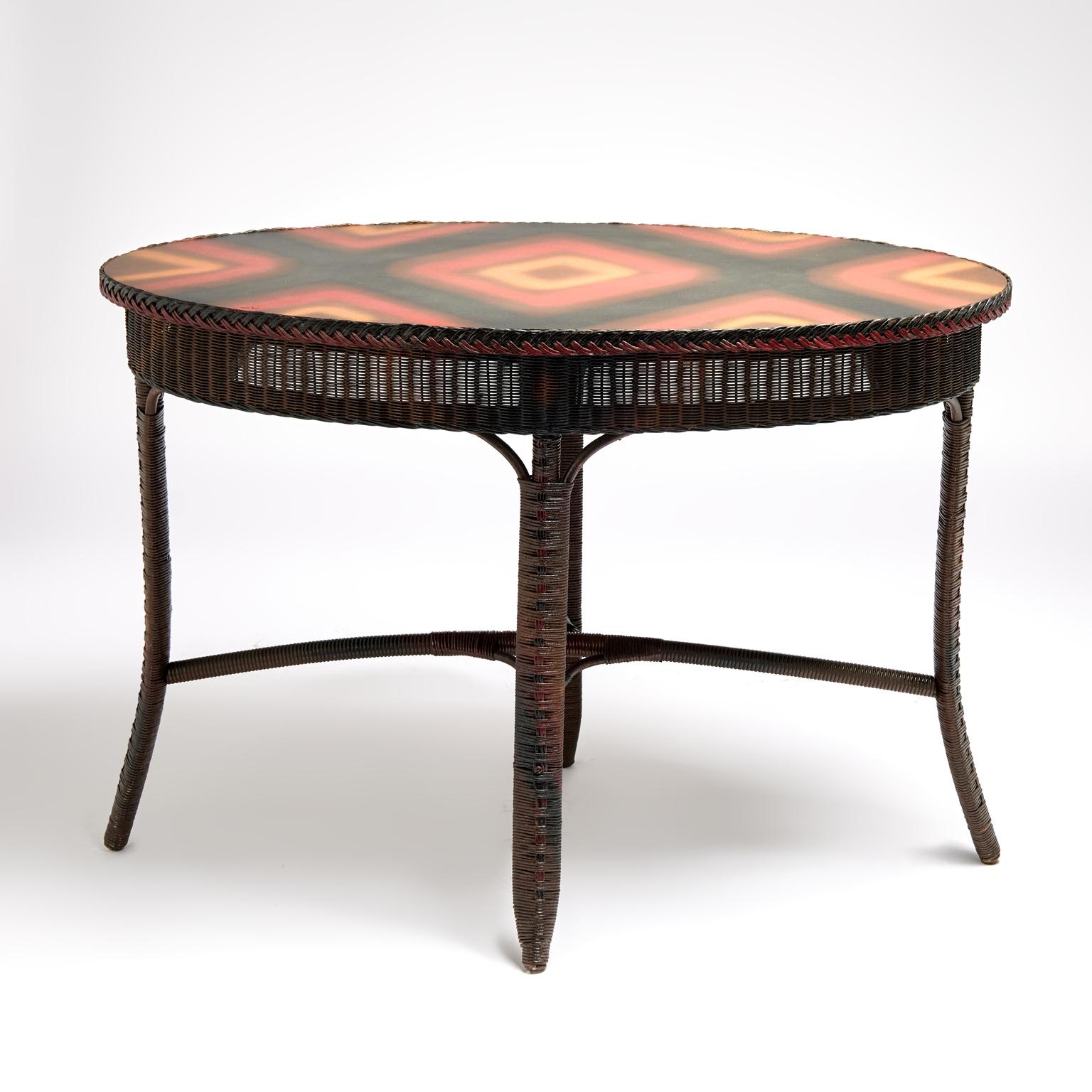 Spirited antique oval table handcrafted in stick wicker and woven reed featuring  the original painted top decorated with an advanced spray technique on four legs with splayed legs joined by cross stretchers. Signed Lloyd Loom on the bottom. 