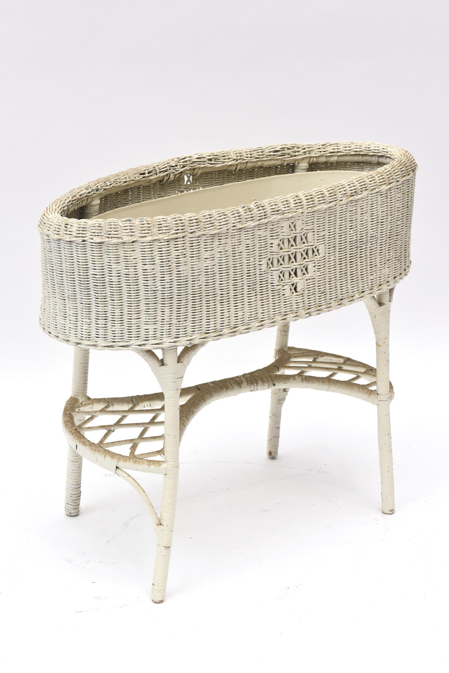 This lovely tightly woven wicker plant stand has an openwork pattern on the sides and an open lattice stretcher beneath which widens on each side to hold a potted plant or perhaps a watering can. A tin liner sits inside to protect the wicker while