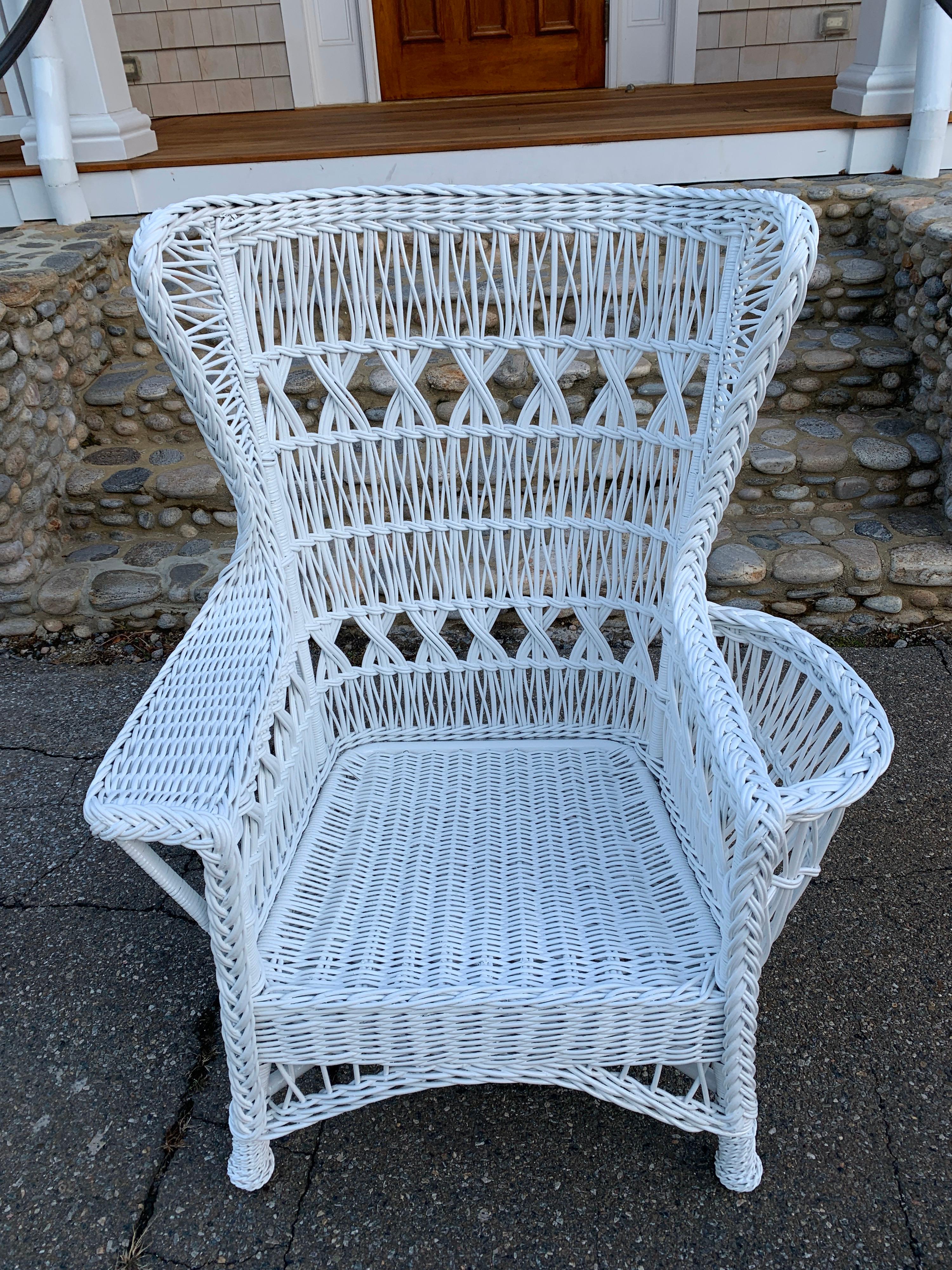 A special antique wicker wingback armchair in the triple cross pattern with magazine pocket and woven feet. Freshly painted white. Chair measures 36