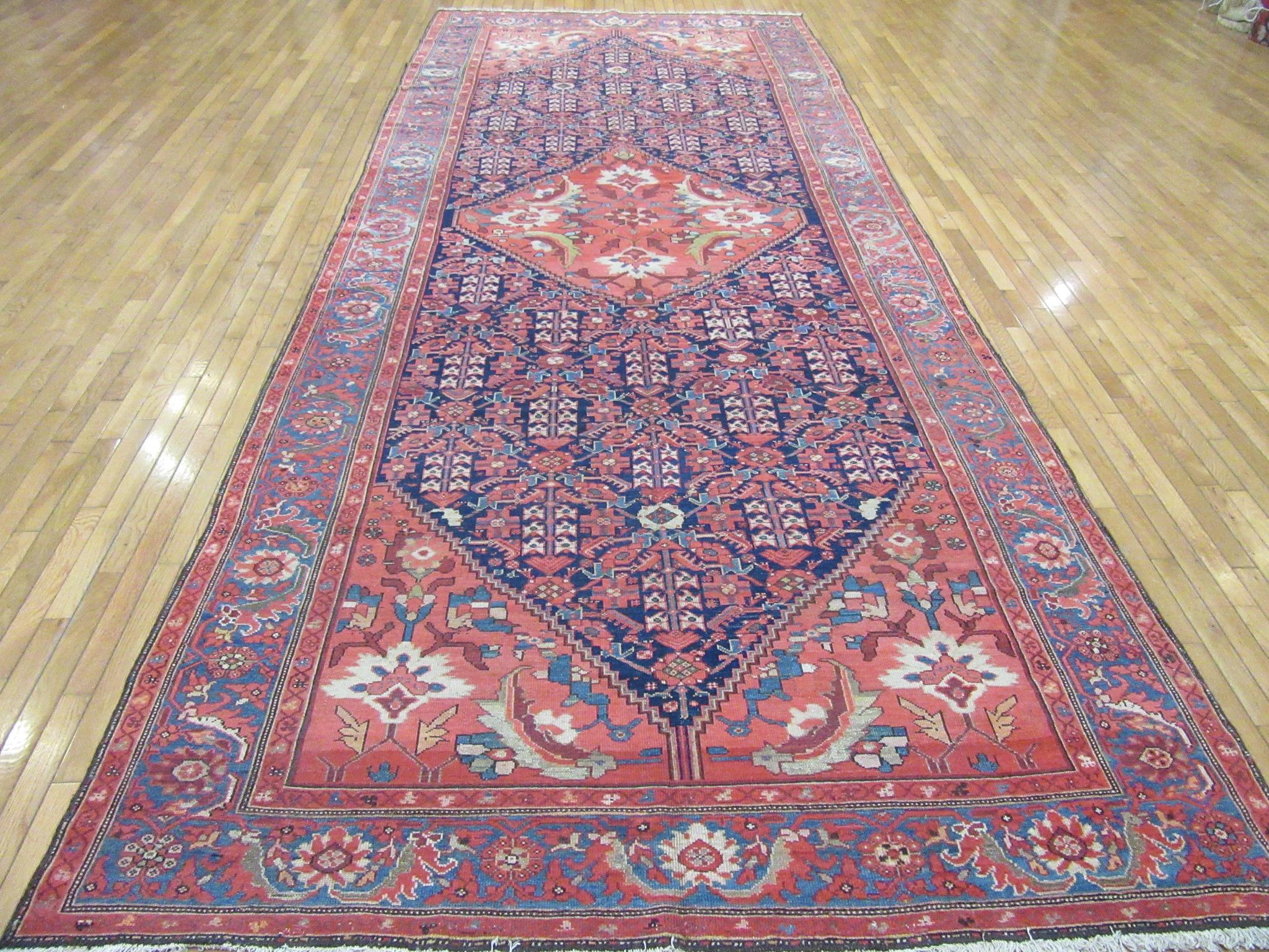 This is an antique hand knotted wool gallery size rug made with wool colored with natural dyes. It has a distinct pattern with a central and corner medallion design on a navy blue background, The rug measures 6' 6