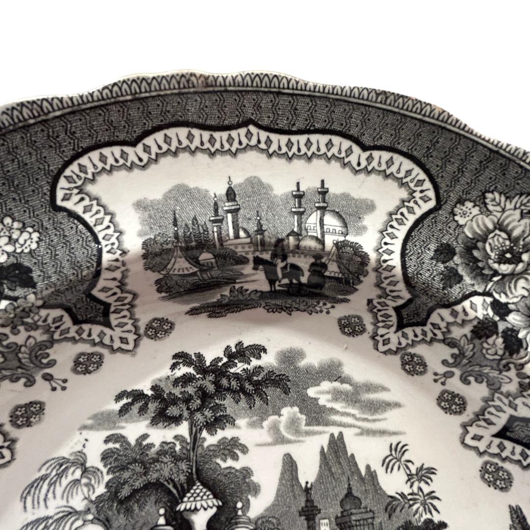 This elegant earthenware bowl from William Adams & Sons made in Staffordshire, England was made during the late 19th century, It has a stopped edge with flowers and architectural buildings along with mountains and people in center. The bowl,