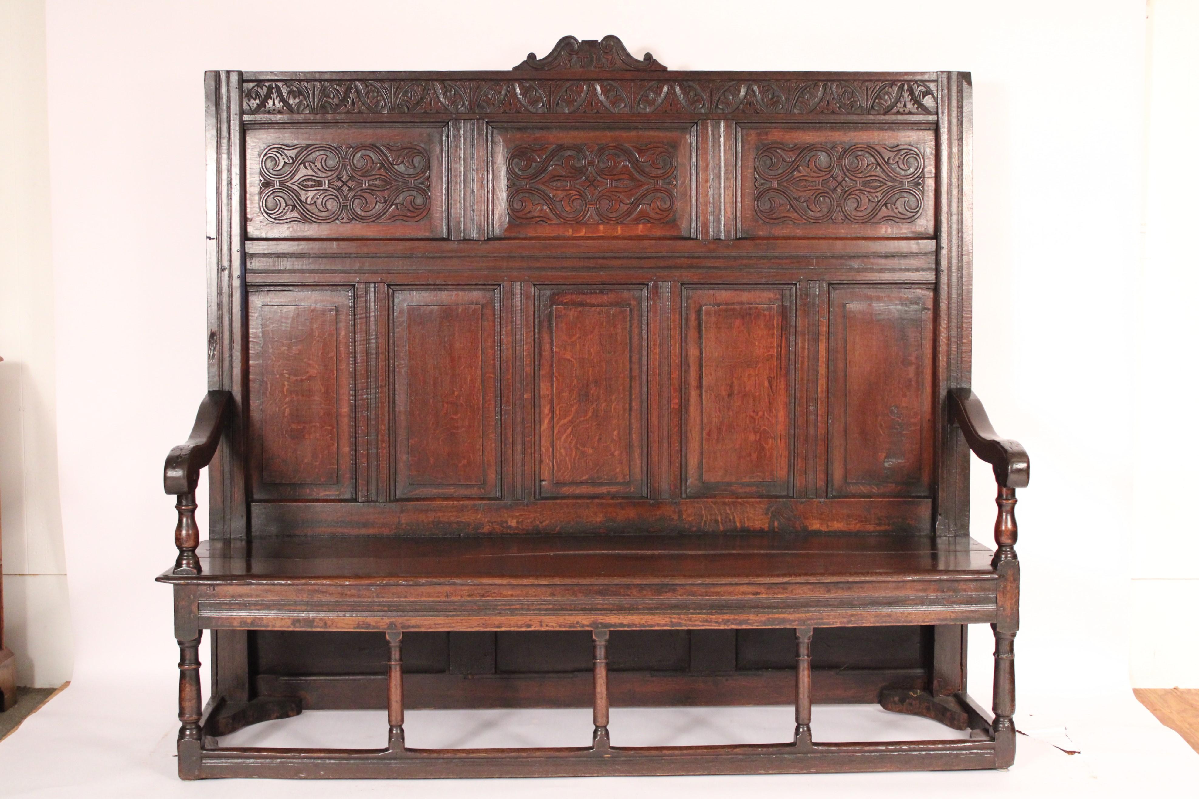 Antico insediamento in quercia in stile William & Mary, XIX secolo. Frontone con iniziali T.L., schienale intagliato e pannellato, braccioli a forma di serpentina, sedile a due assi, gambe tornite unite da barelle. Costruzione a tenone e pioli. Una
