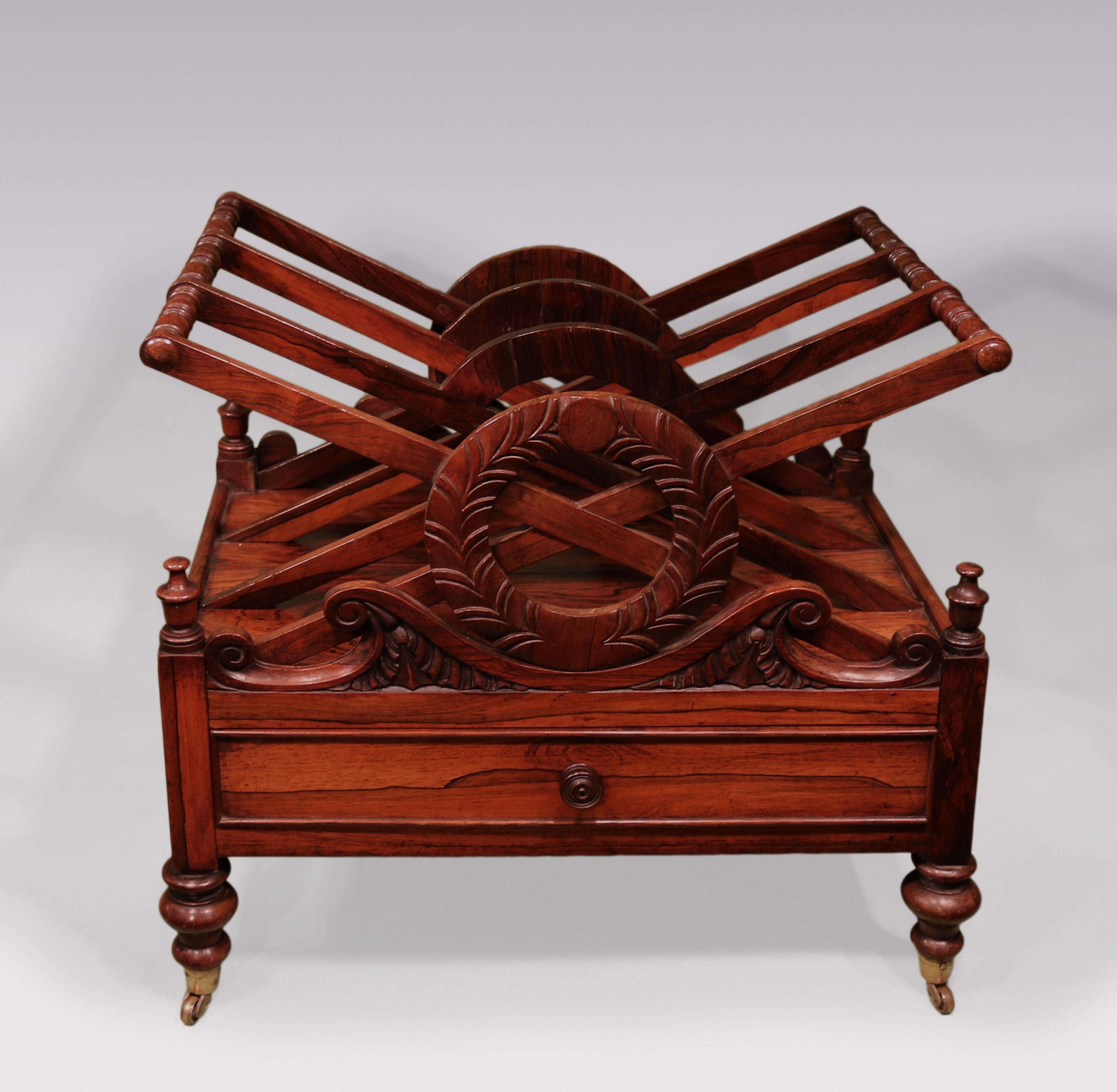 A William IV rosewood 3-section X framed Canterbury having carved & scrolled wreath front & back and frieze drawer, supported on turned legs ending on original brass castors.