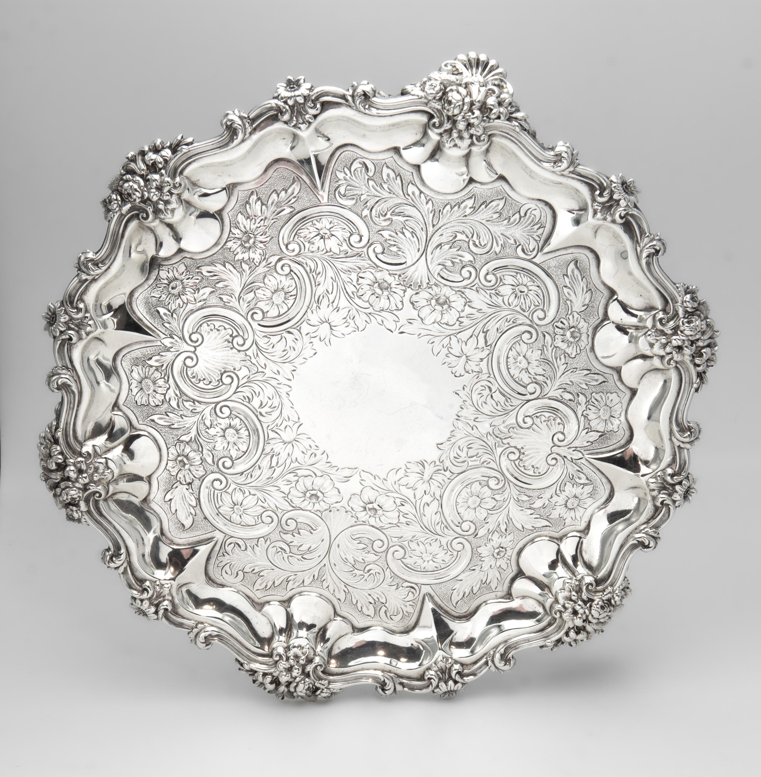 Antique William IV sterling silver flat-chased waiter, hallmarked London, 1831, by makers Edward, Edward Jr, John and W. Barnard.

The decorative waiter has a scroll and foliate cast rim with alternating flowers against rocaille, standing on cast